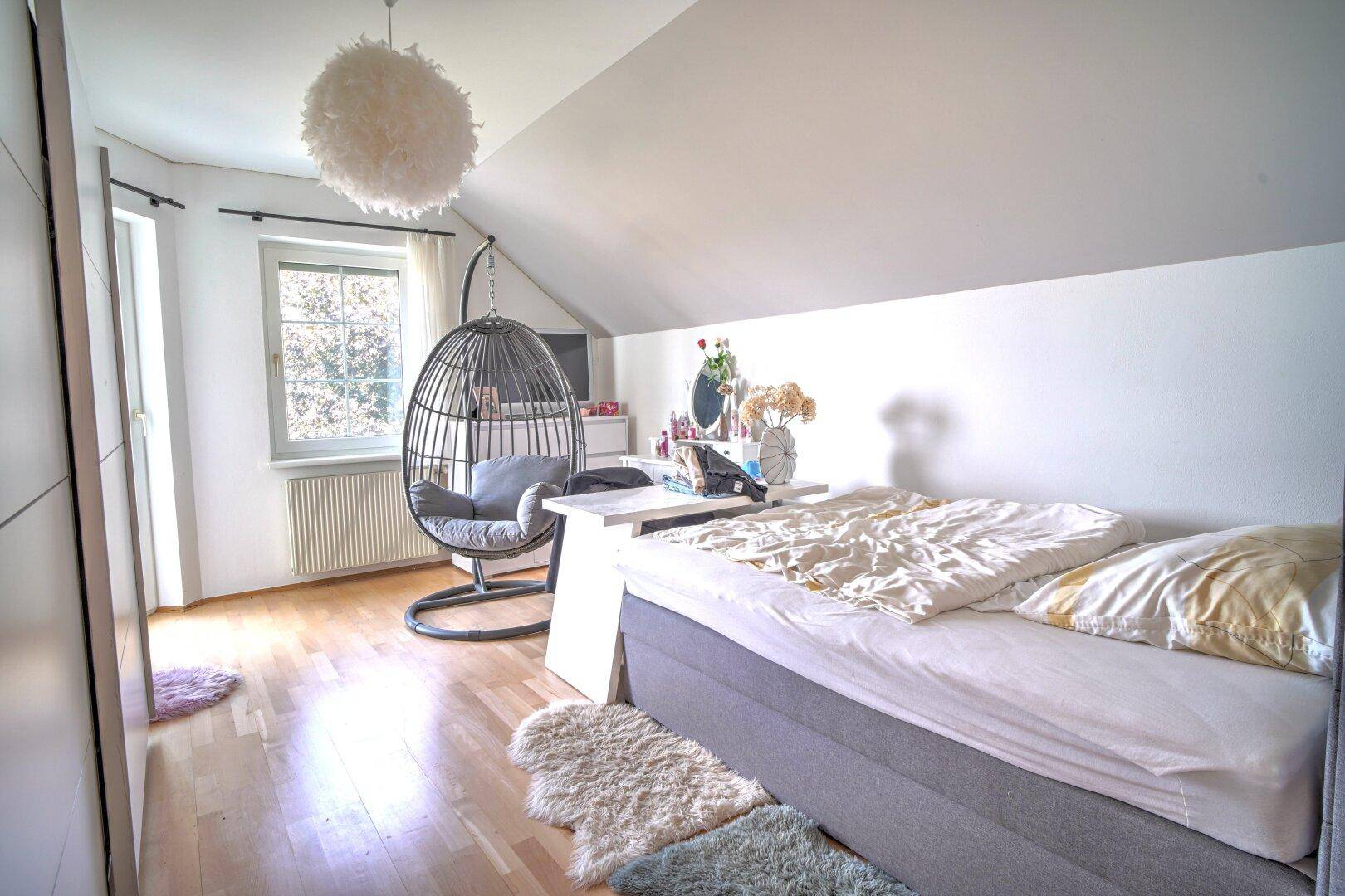 Gemütliches Schlafzimmer unter der Dachschräge mit Holzboden und Fenster.