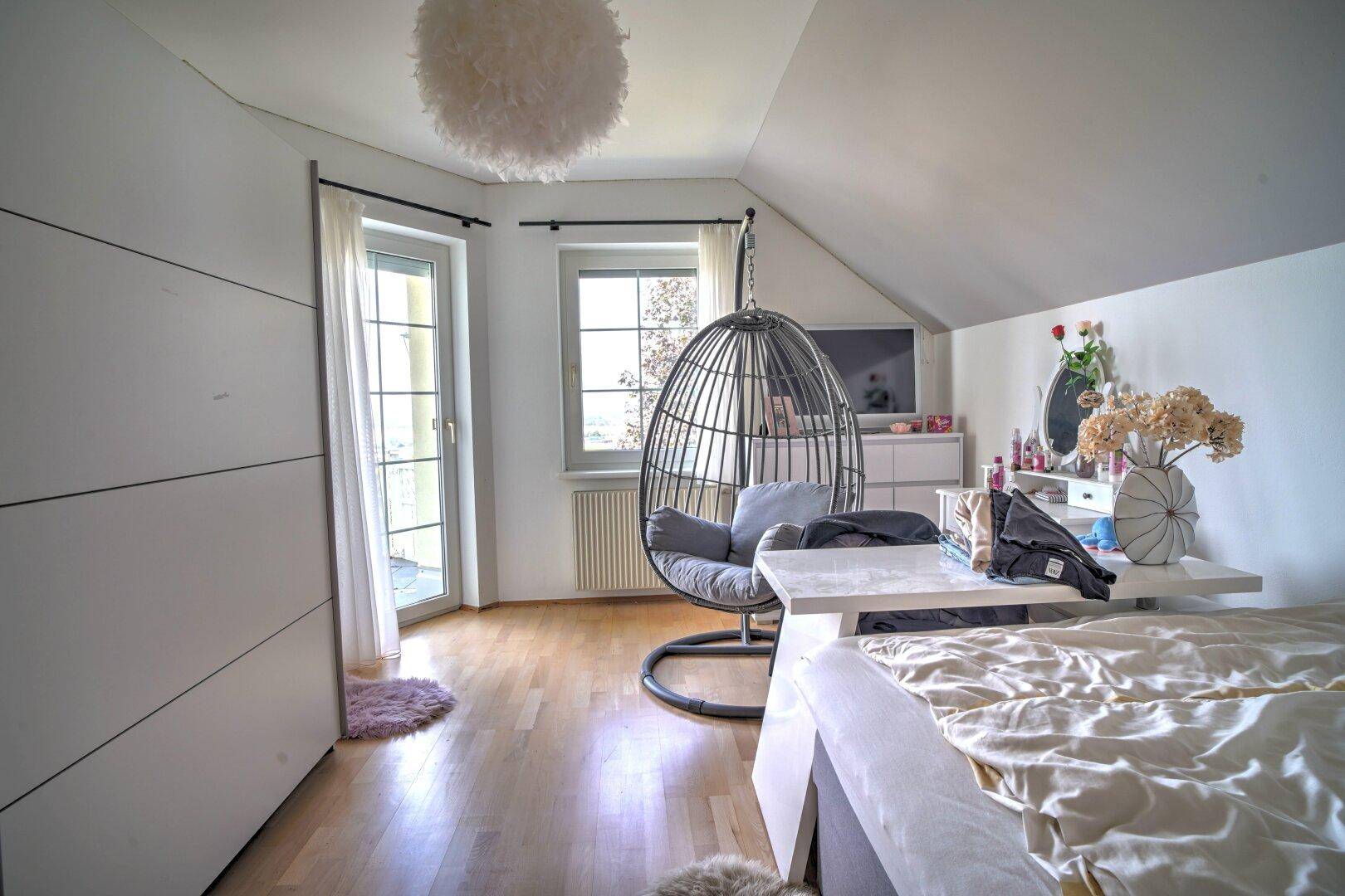 Helles Schlafzimmer unter der Dachschräge mit Holzboden und Zugang zu einem französischen Balkon.