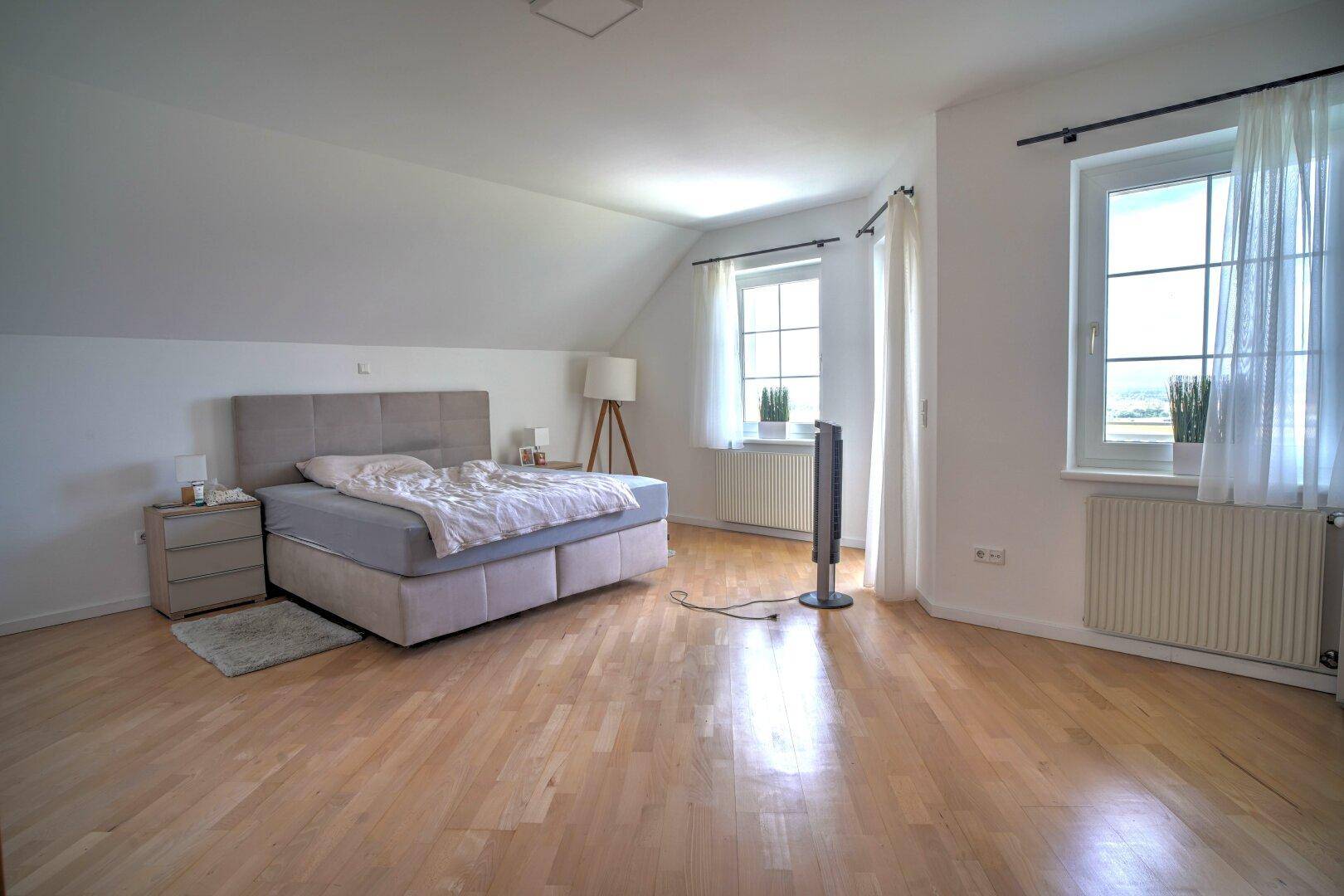 Großes Schlafzimmer unter der Dachschräge mit Holzboden und zwei Fenstern.
