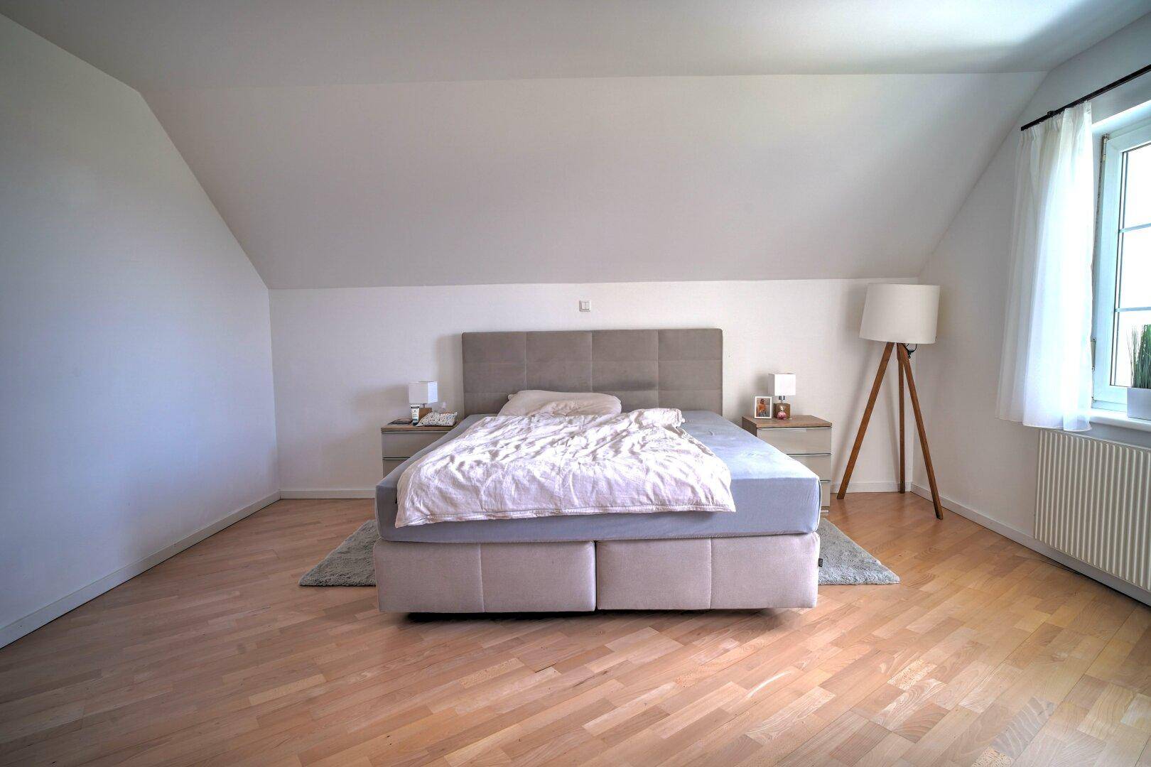 Helles Schlafzimmer unter der Dachschräge mit Holzboden und großem Bett.