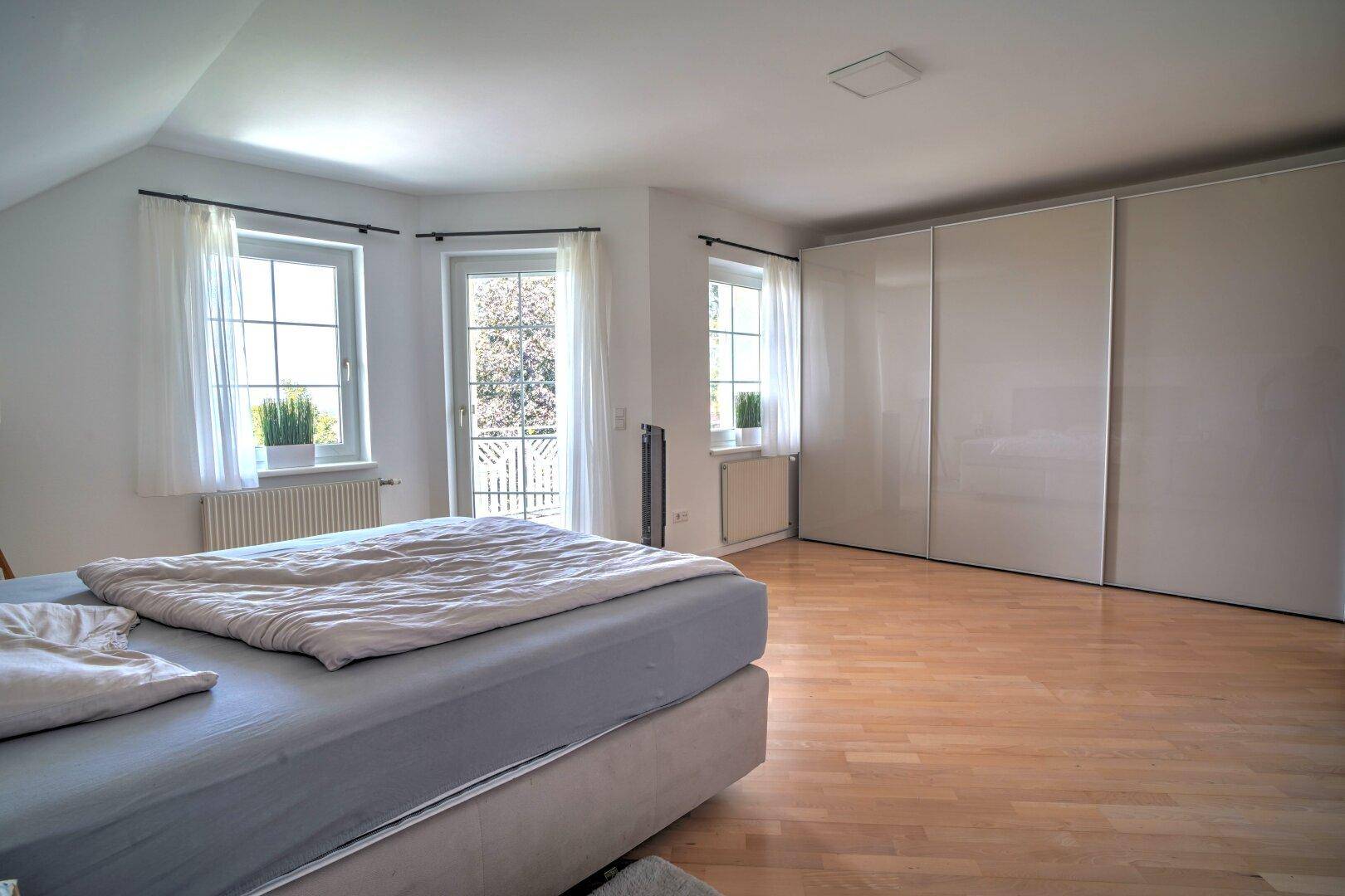 Geräumiges Schlafzimmer unter der Dachschräge mit Einbauschränken und Zugang zum französischen Balkon.