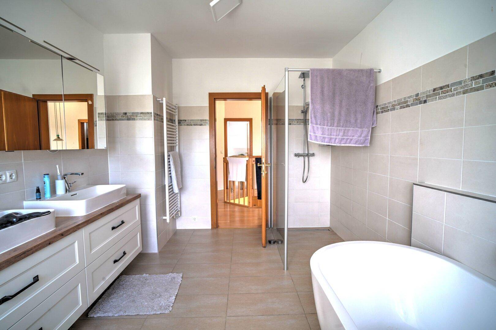 Elegantes Badezimmer mit freistehender Badewanne, Dusche, Doppelwaschbecken und beheiztem Handtuchhalter.