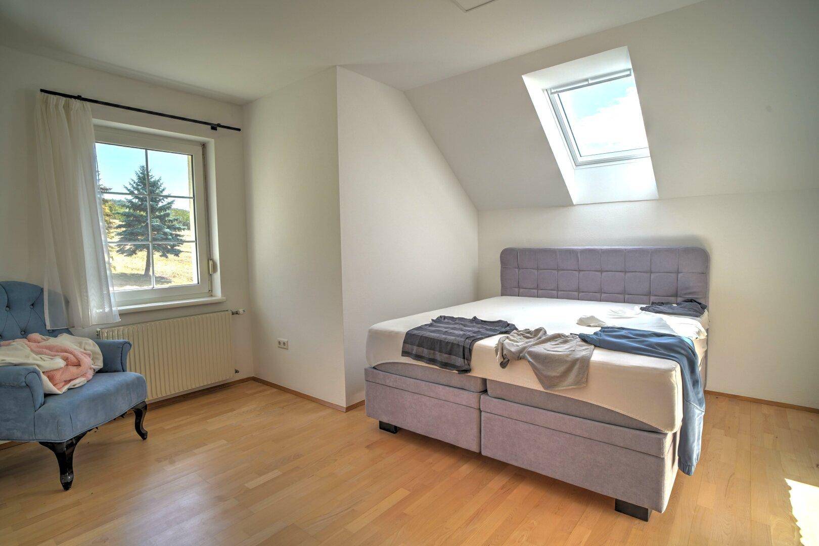 Helles Schlafzimmer unter der Dachschräge mit Holzboden, Fenster und Dachfenster.