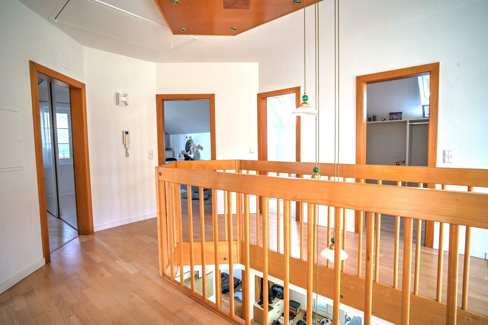 Heller Flur im Obergeschoss mit Holzboden, Holzgeländer und dekorativer Deckenleuchte.