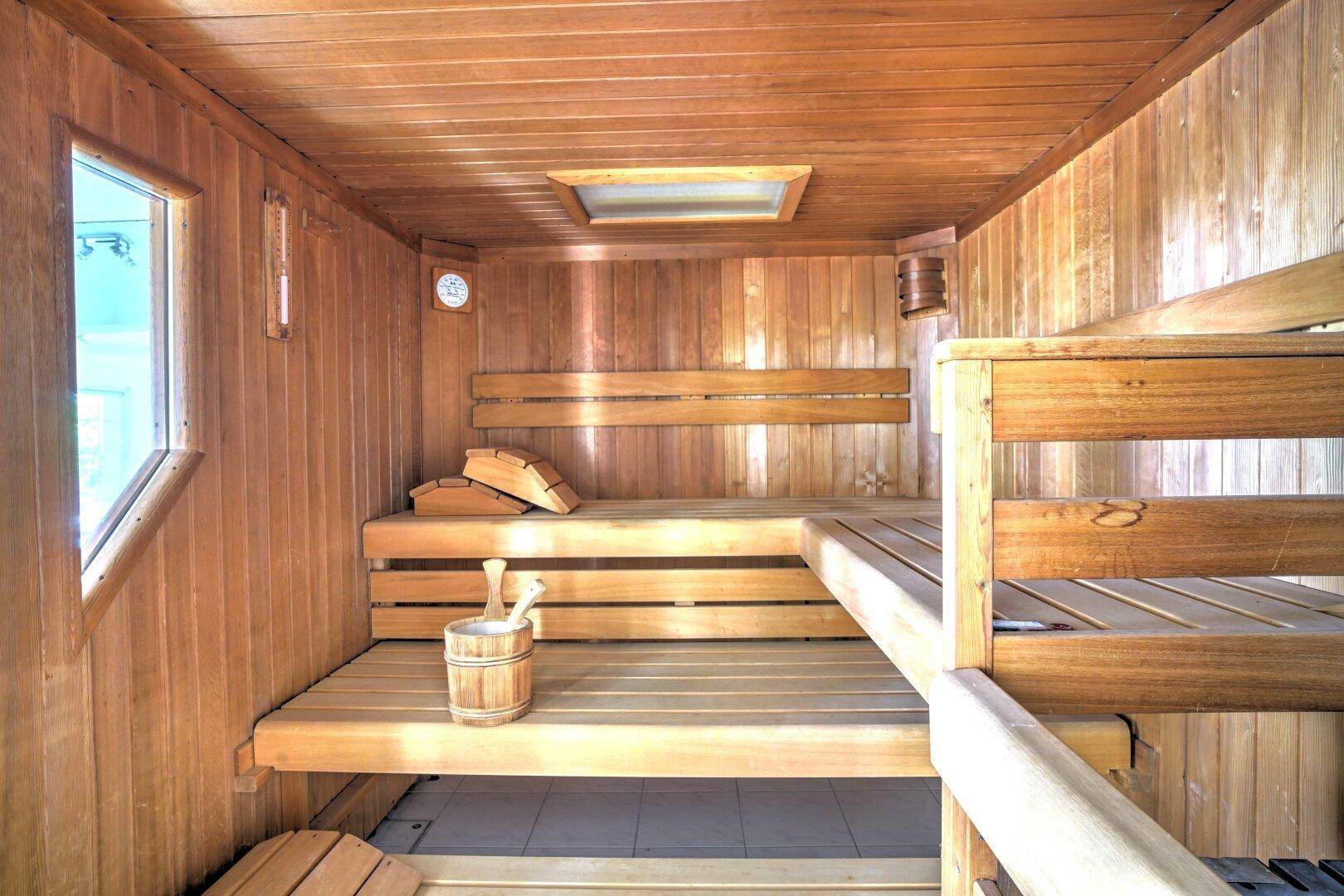 Traditionelle Holzsauna mit mehreren Bänken und klassischem Zubehör für Entspannung.