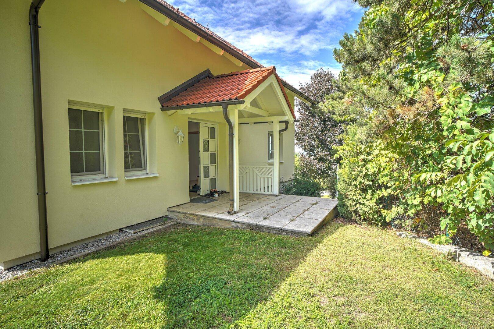 Eingangsbereich des Hauses mit überdachtem Vordach und gepflegtem Rasen in sonniger Umgebung.