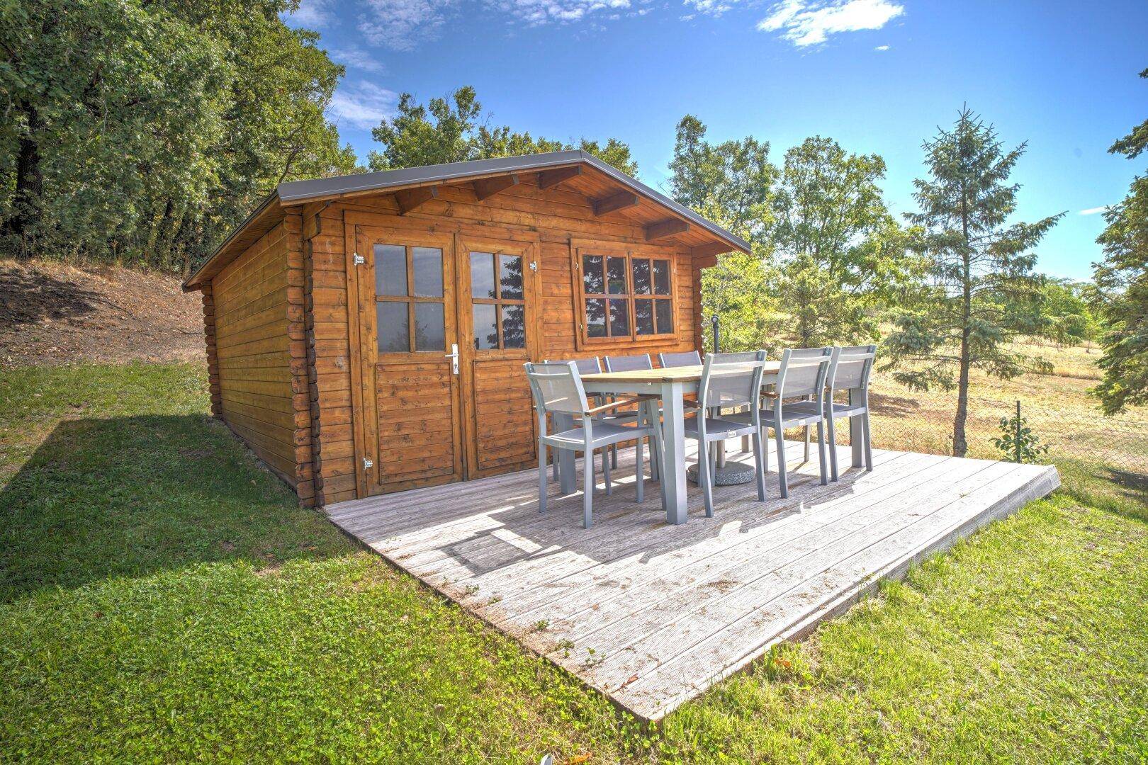 Charmante Holzhütte mit einer einladenden Terrasse und Gartenmöbeln, umgeben von grüner Landschaft.