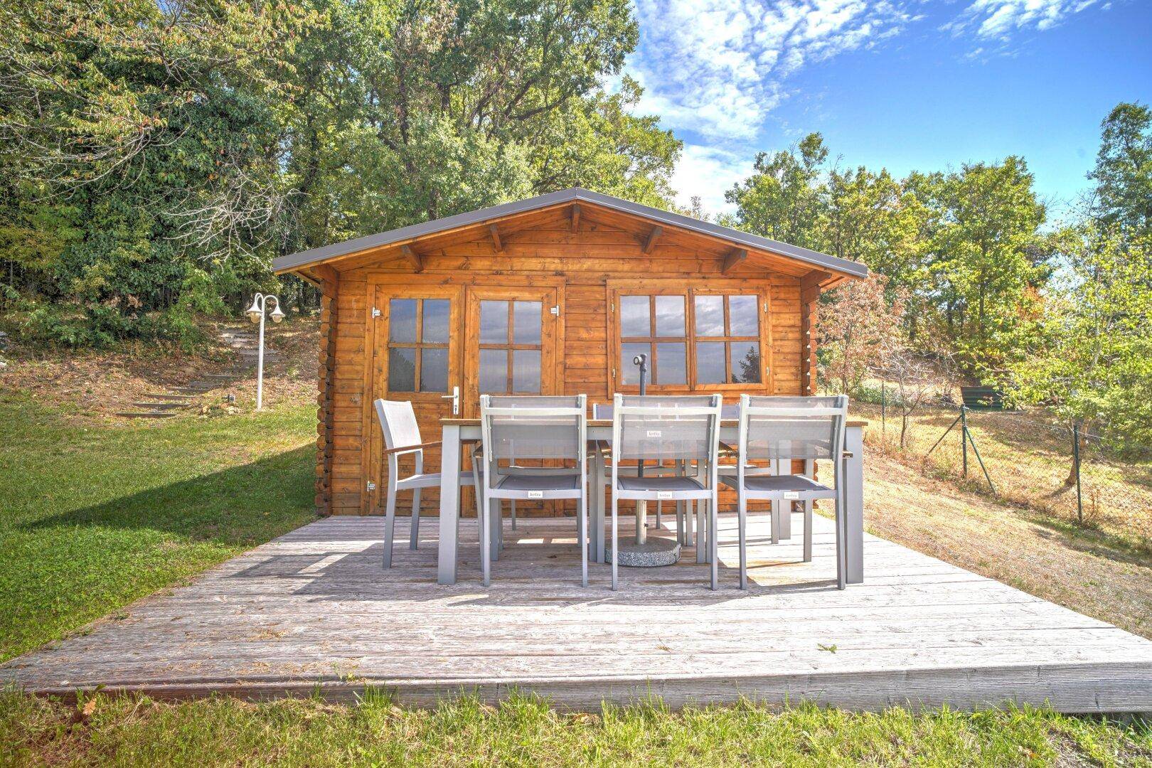 Rustikale Holzhütte mit einer möblierten Holzterrasse, ideal für Mahlzeiten im Freien inmitten der Natur.
