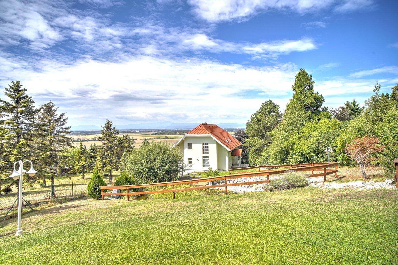 Weitläufiges Grundstück mit einem charmanten Haus, umgeben von Rasenflächen und Bäumen mit Fernblick.
