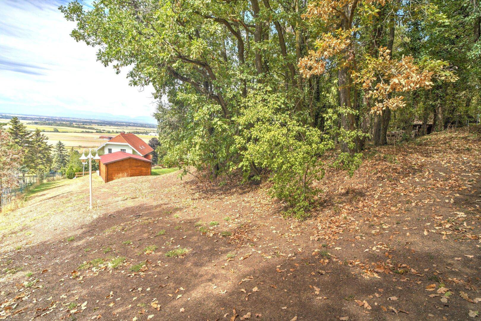 Malerischer Blick von einem erhöhten Punkt auf das Haus und die weite Landschaft, umgeben von Bäumen.