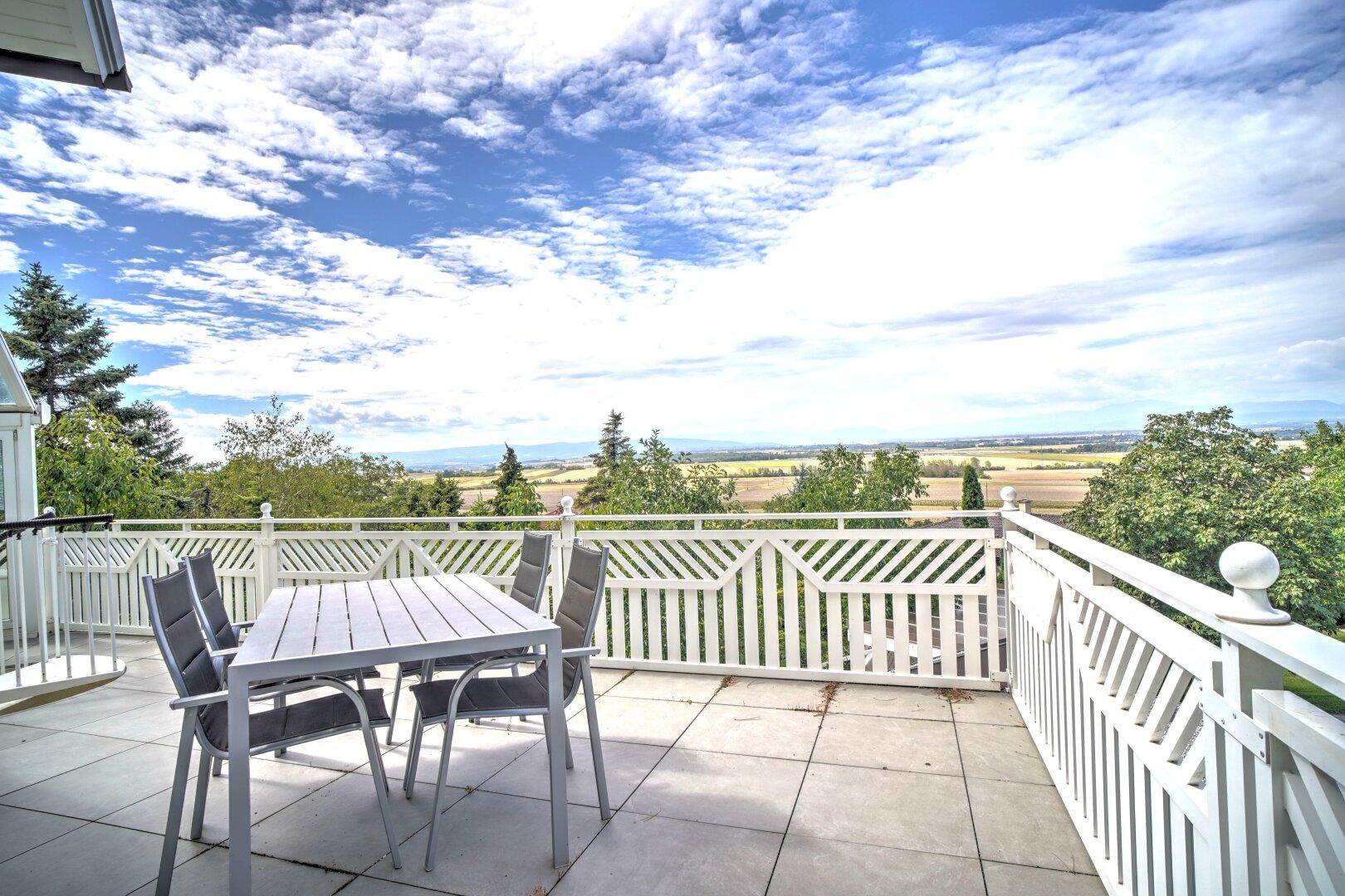 Geräumige Terrasse mit weißem Geländer und Esstisch, die einen weiten Panoramablick über die Landschaft bietet.