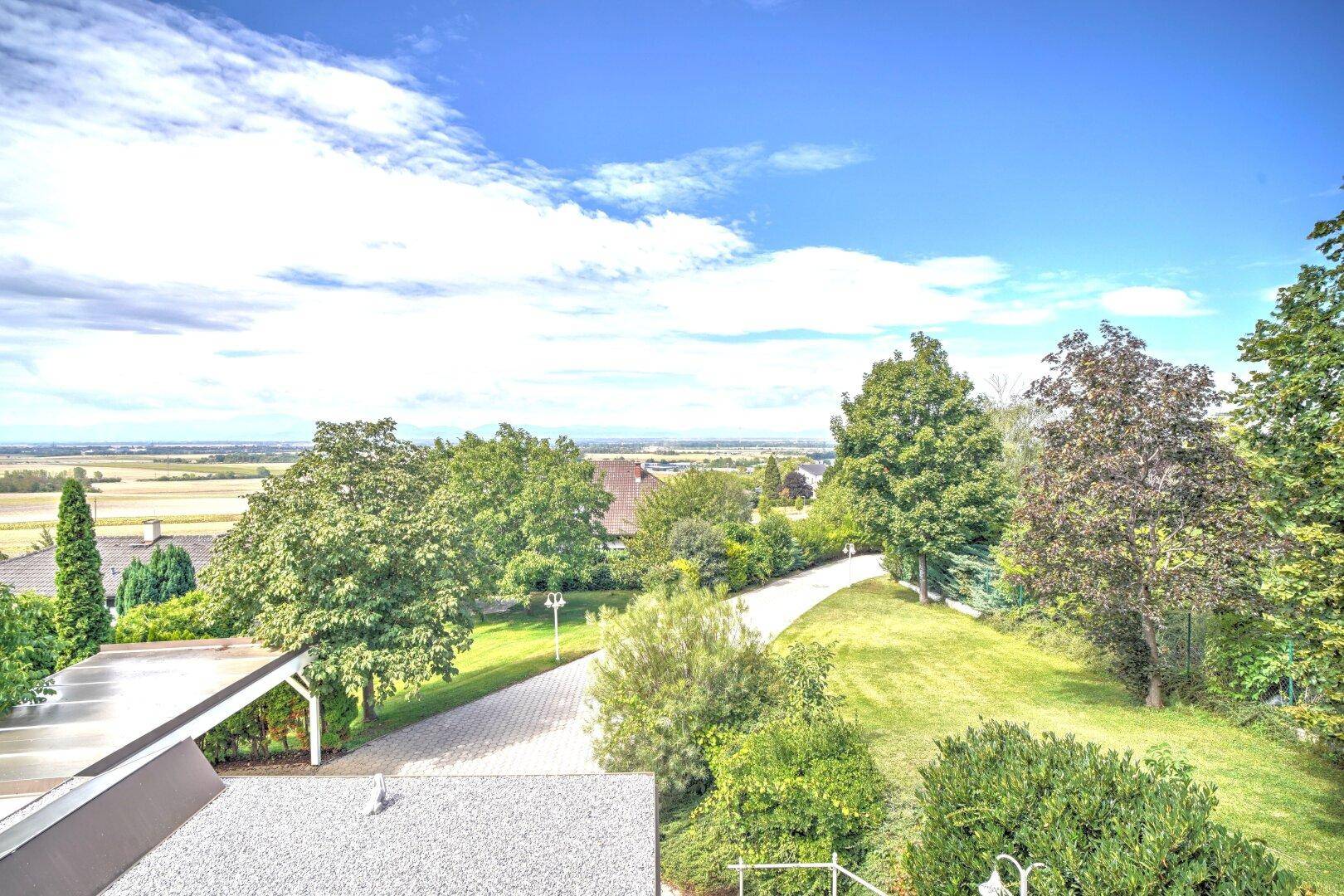 Weitläufige Auffahrt umgeben von Rasenflächen und Bäumen, mit einem Blick auf die umliegende Landschaft.