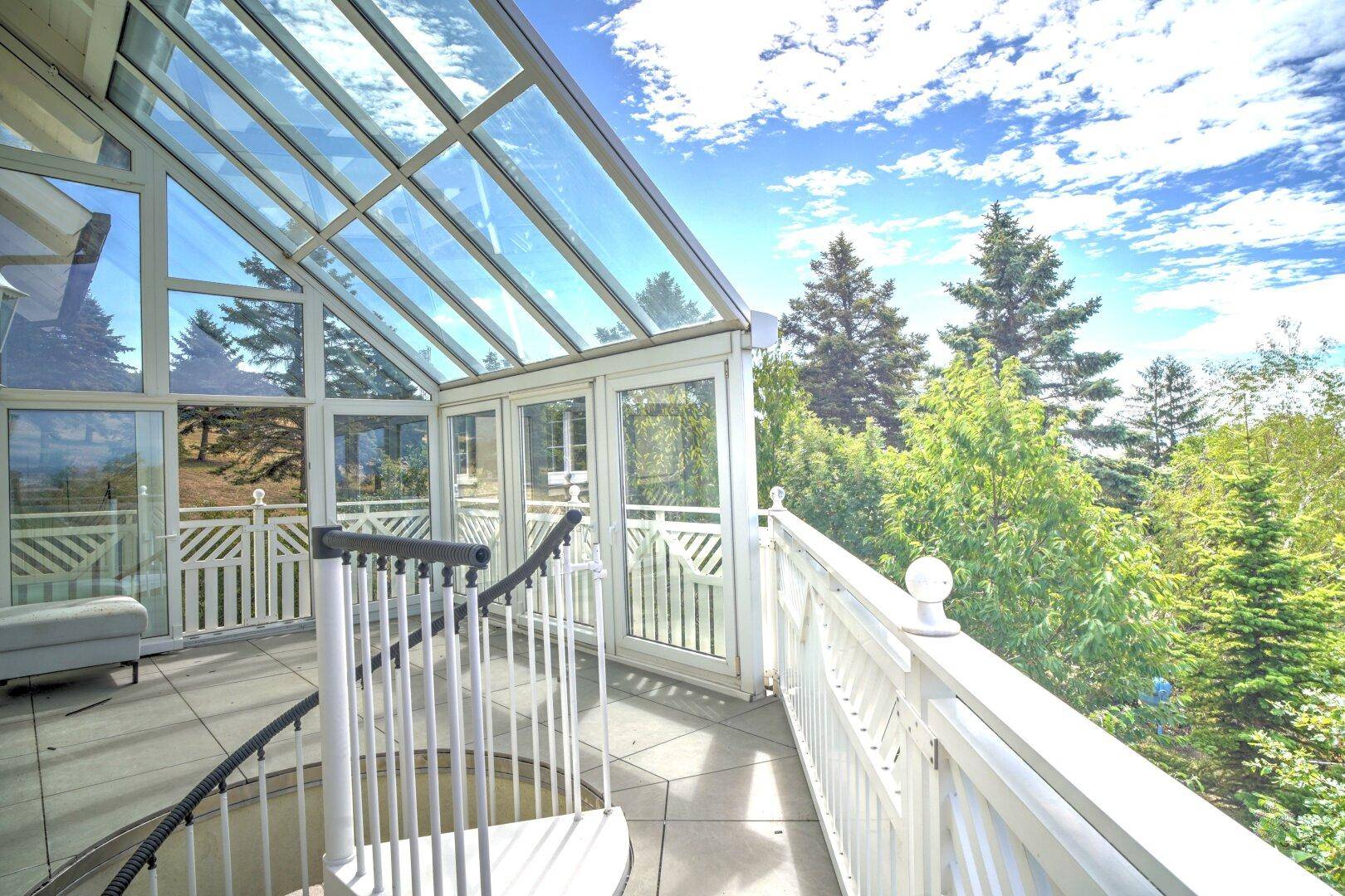 Heller Wintergarten mit Glasdach und Zugang zu einer Terrasse, die einen weiten Blick ins Grüne bietet.