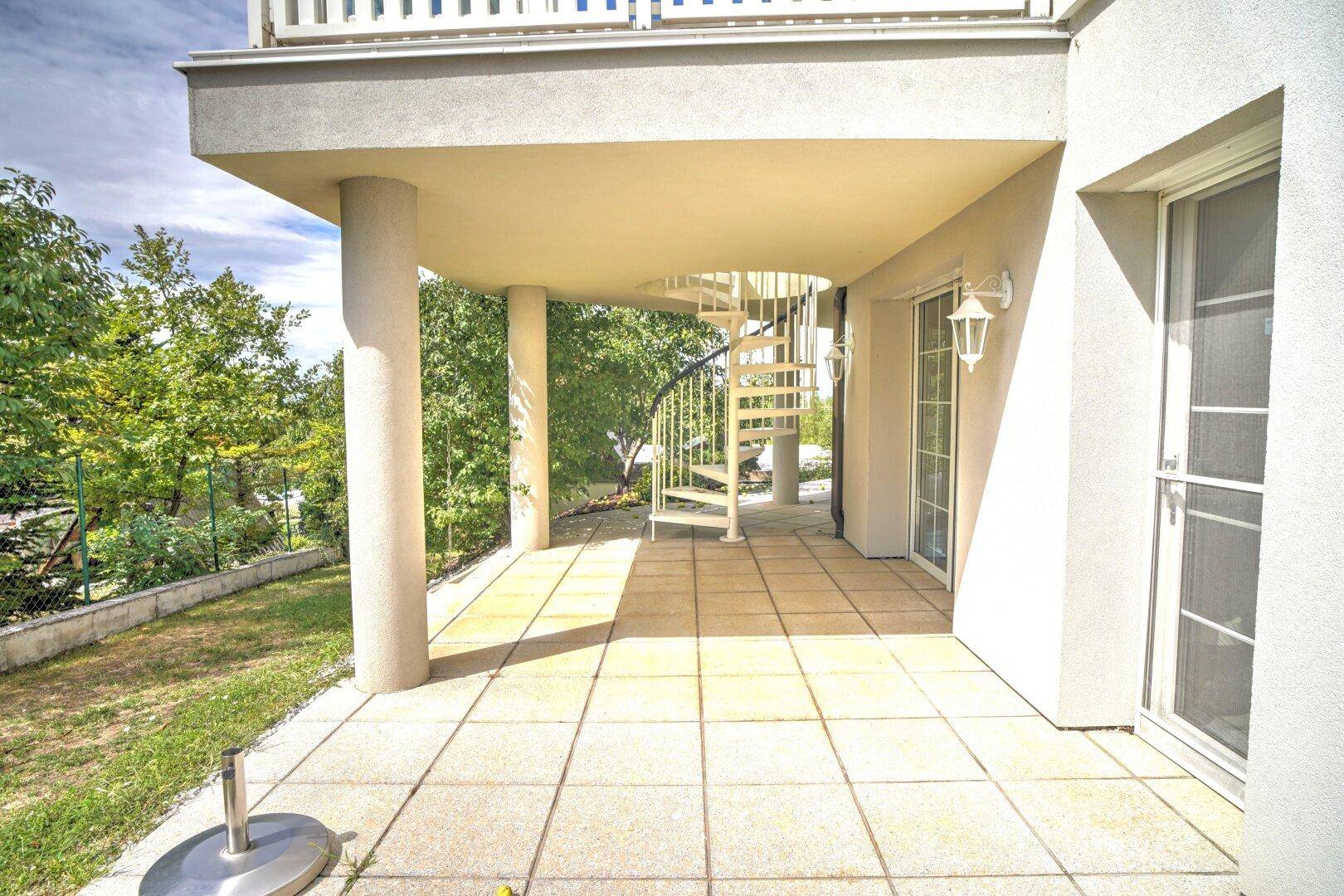 Überdachte Terrasse im Erdgeschoss mit Fliesenboden und einer eleganten Wendeltreppe nach oben.