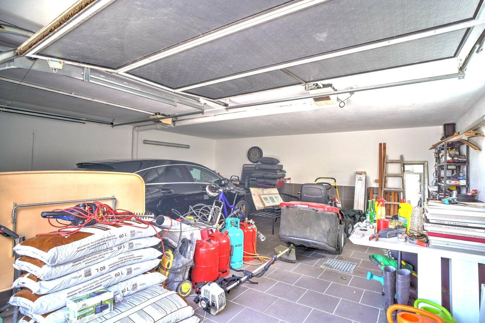 Geräumige Garage, die als Abstellraum dient, mit einem geparkten Auto und verschiedenen Gegenständen.