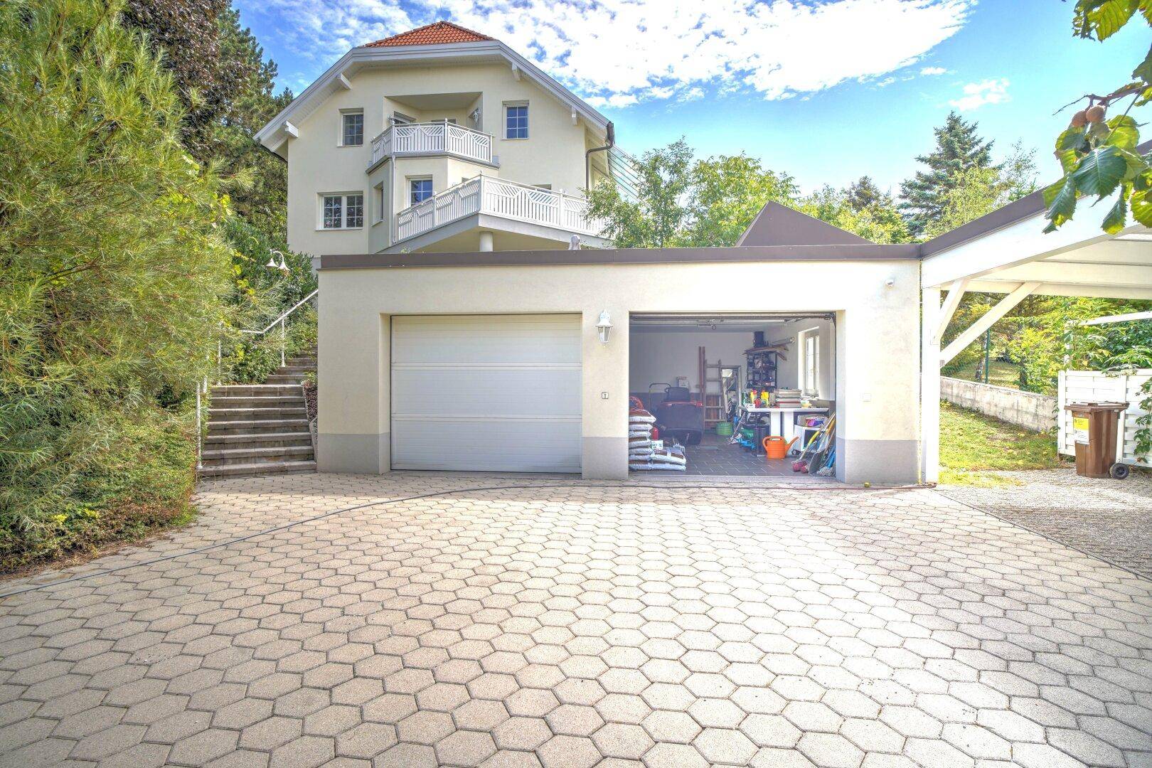 Doppelgarage und Carport mit gepflasterter Auffahrt, das Haupthaus ist im Hintergrund auf dem Hügel sichtbar.