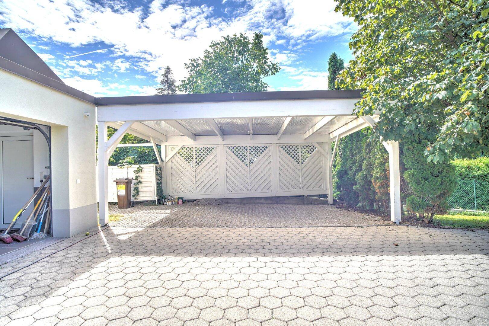Heller Carport mit stabiler Holzkonstruktion und gepflastertem Boden, bietet geschützten Parkraum.