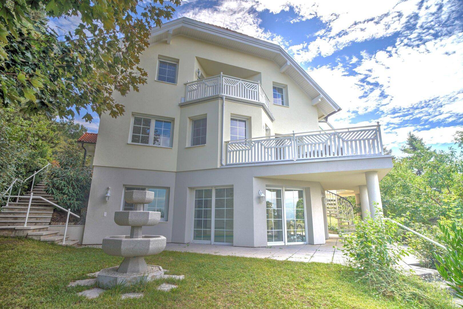 Mehrstöckiges Haus mit mehreren Balkonen und einer kleinen Steinfassade im Vorgartenbereich.