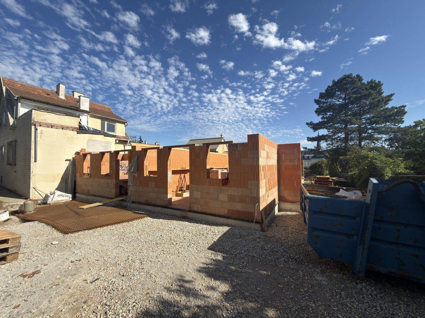 Baustelle eines Neubaus mit bereits errichteten Ziegelwänden unter blauem Himmel.