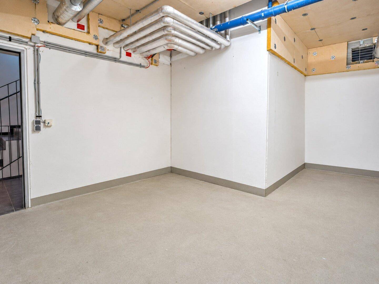 Lagerraum im Keller mit sichtbaren Rohren an der Decke und grauem Boden.