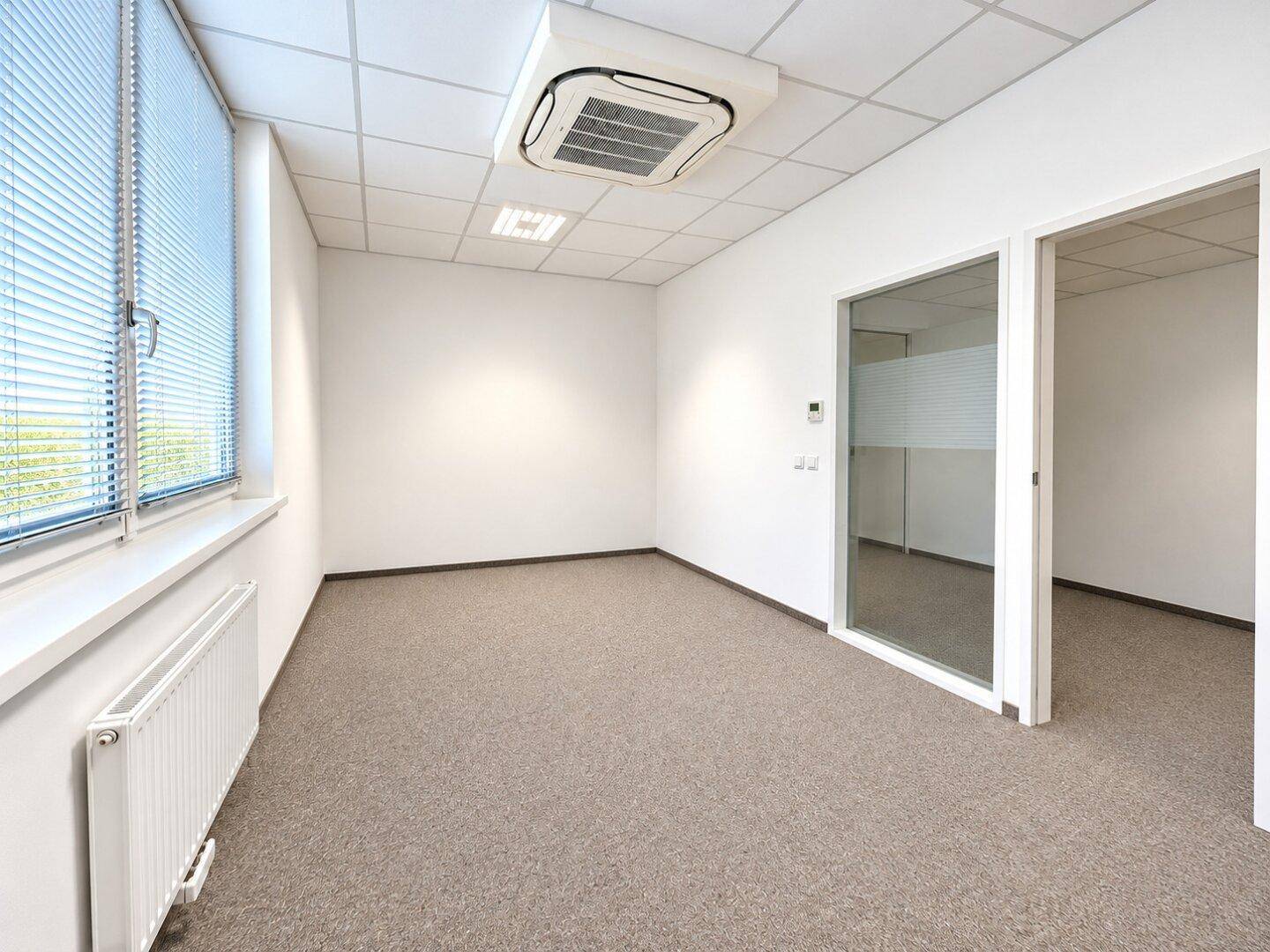 Leeres Büro mit Teppichboden, Fenster mit Jalousien und Deckenklimaanlage.
