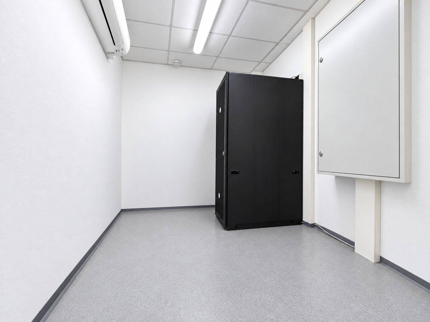 Serverraum mit schwarzem Serverschrank, weißen Wänden und Klimaanlage.