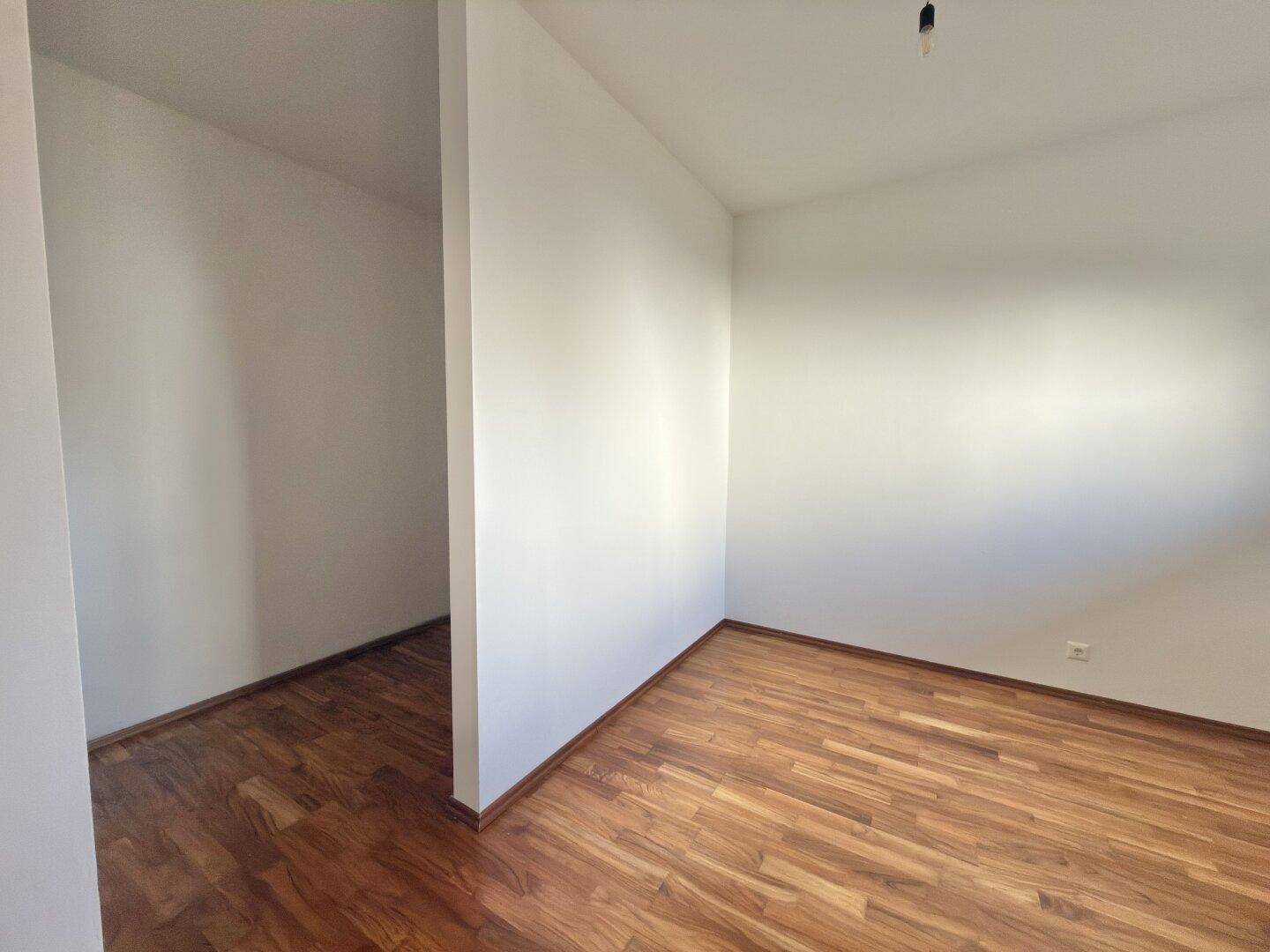 Helles Zimmer mit Holzboden und weiß gestrichenen Wänden, bereit zur individuellen Einrichtung.