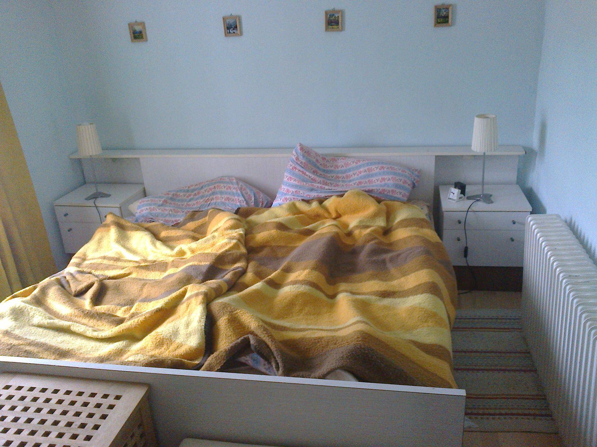 Schlafzimmer mit Doppelbett, Nachttischen und hellblauen Wänden, gut beleuchtet.