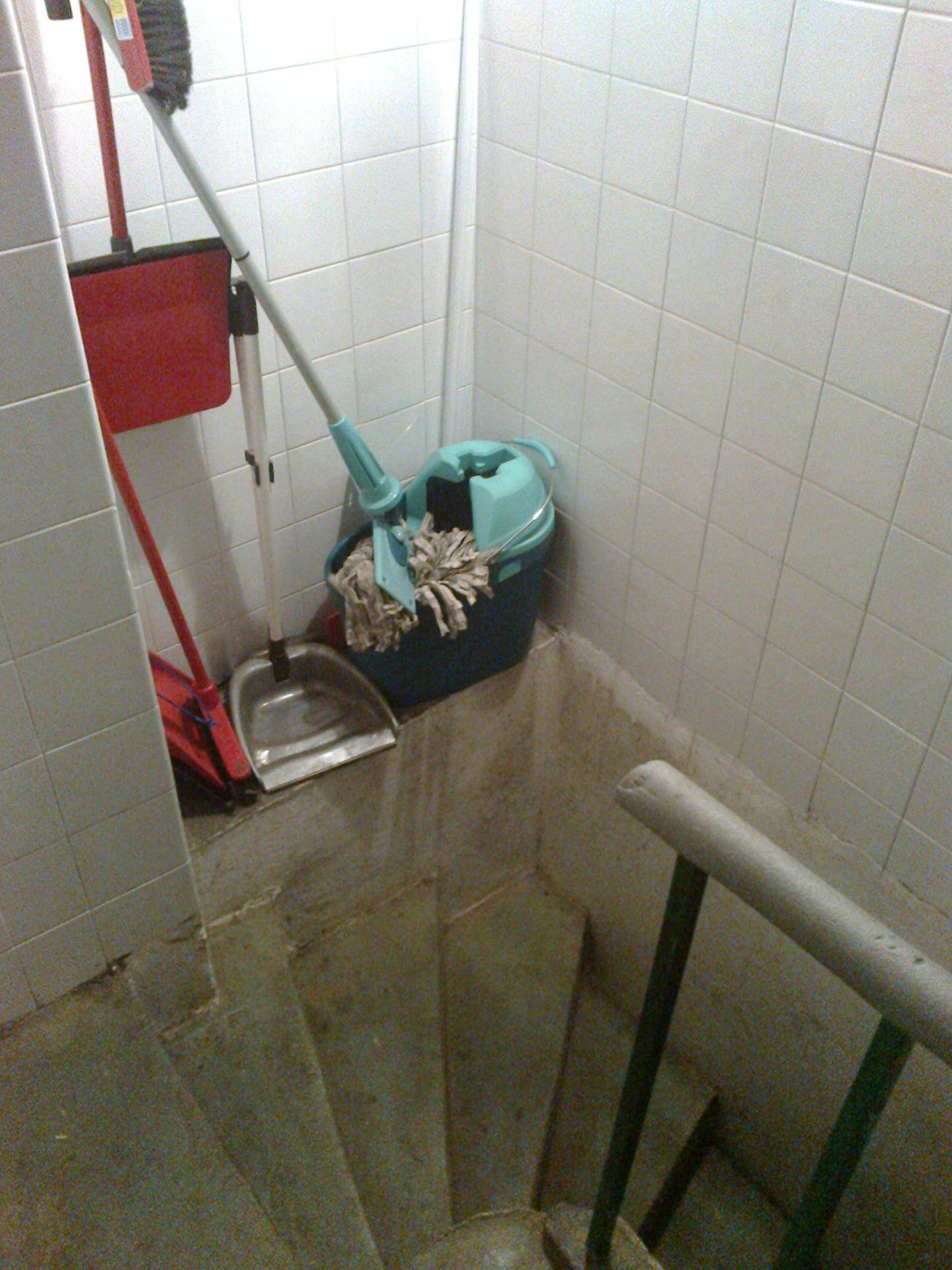 Betontreppe mit Reinigungsutensilien in einem gefliesten Bereich, möglicherweise im Keller.