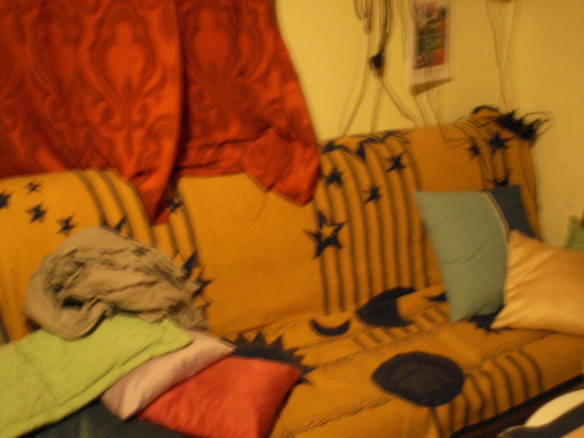 Gemütliches Sofa mit vielen bunten Kissen und einem roten Vorhang im Hintergrund.