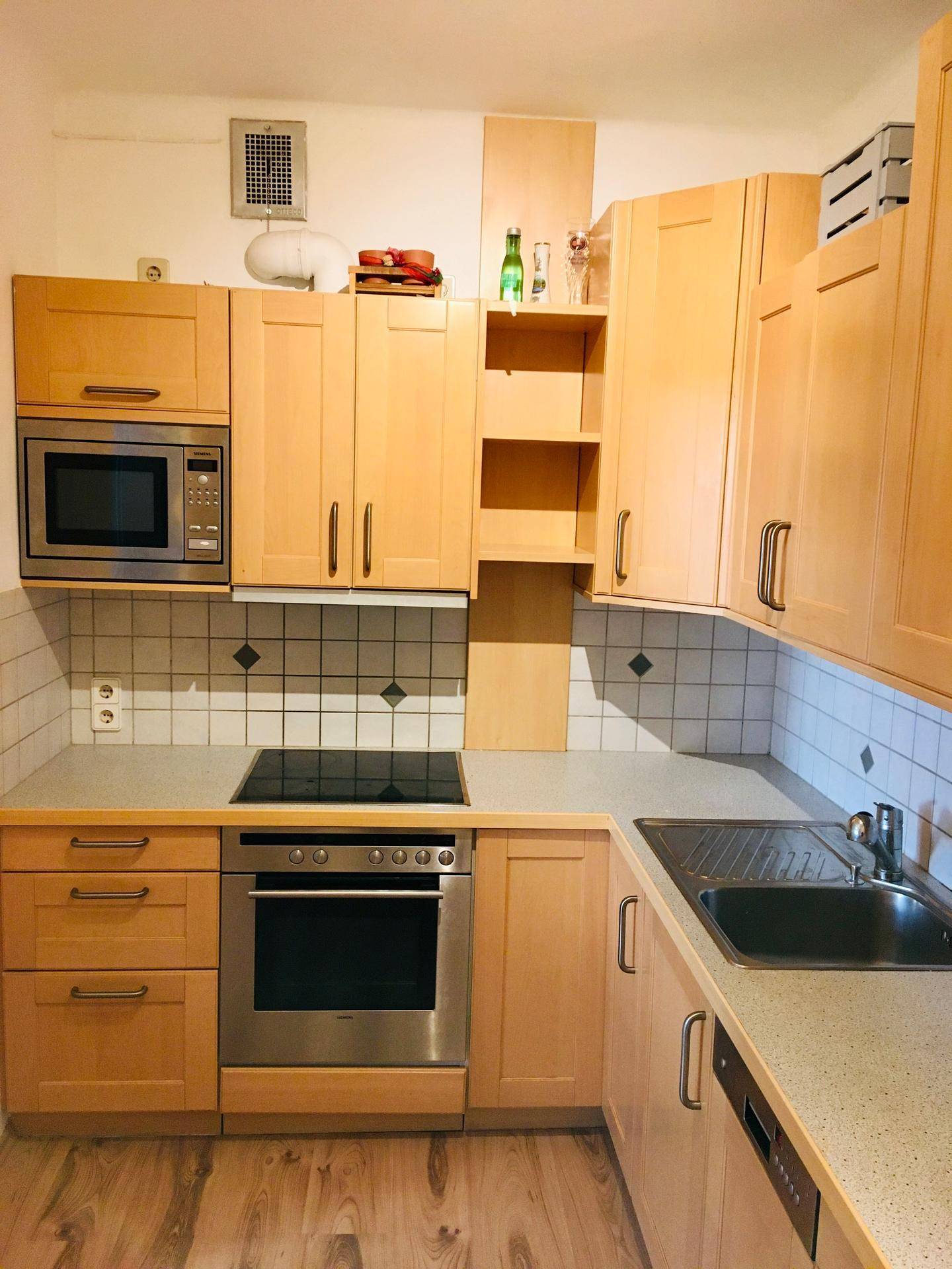 Funktionale Küche mit hellen Holzschränken, integriertem Backofen, Mikrowelle und Kochfeld.