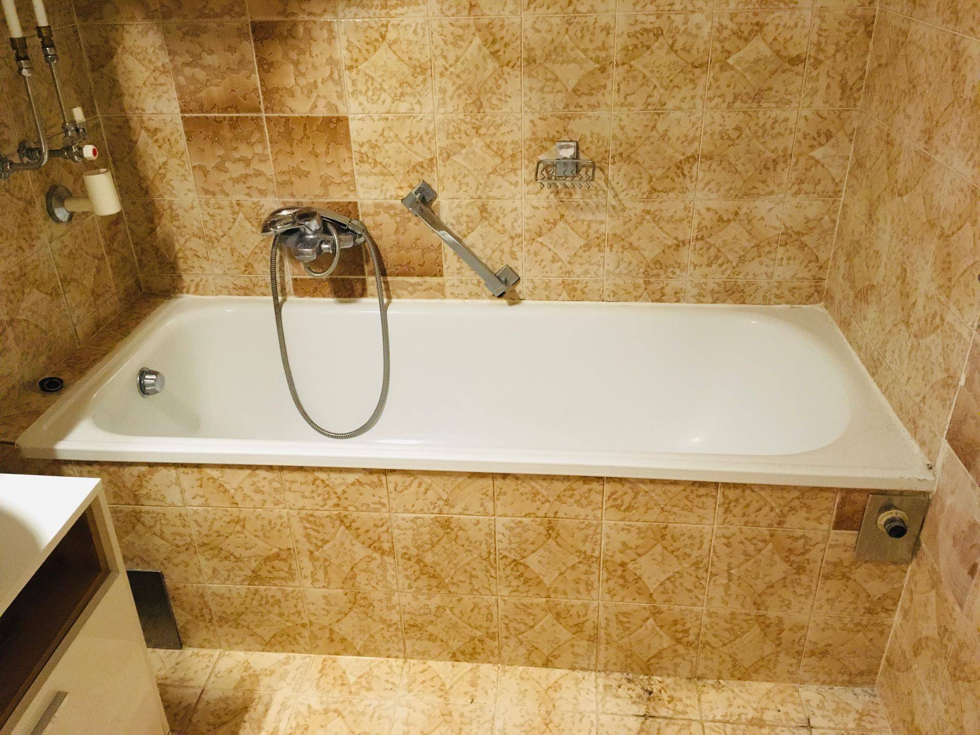 Badezimmer mit Badewanne und gemusterten Fliesen an Wänden und Boden.