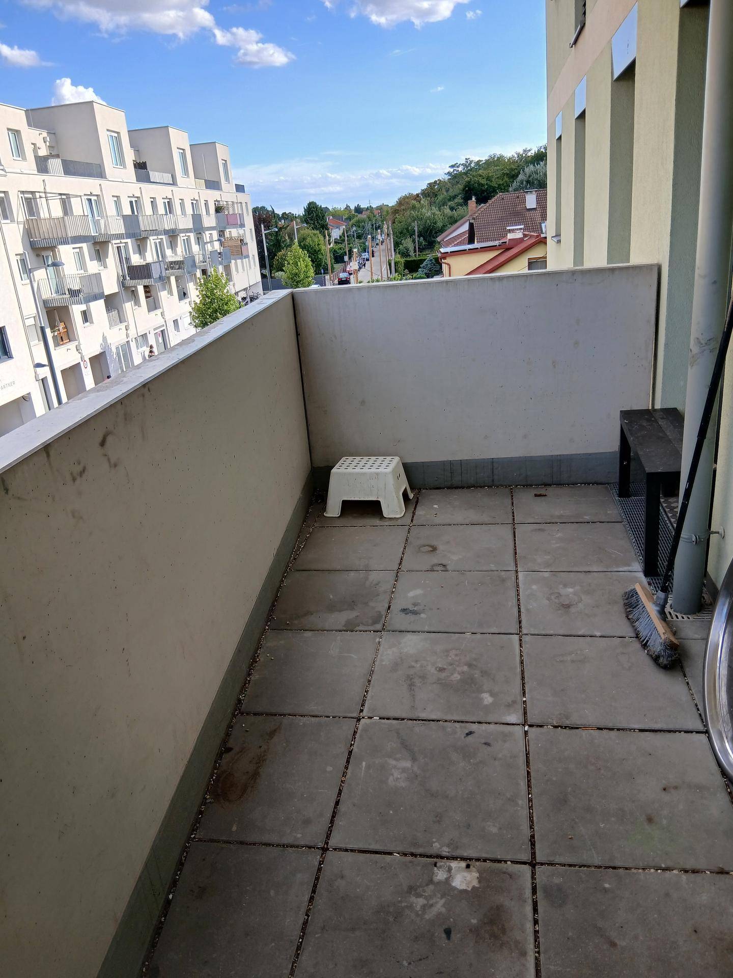 Kleiner Balkon mit Fliesenboden und Blick auf die umliegenden Gebäude und die Straße.