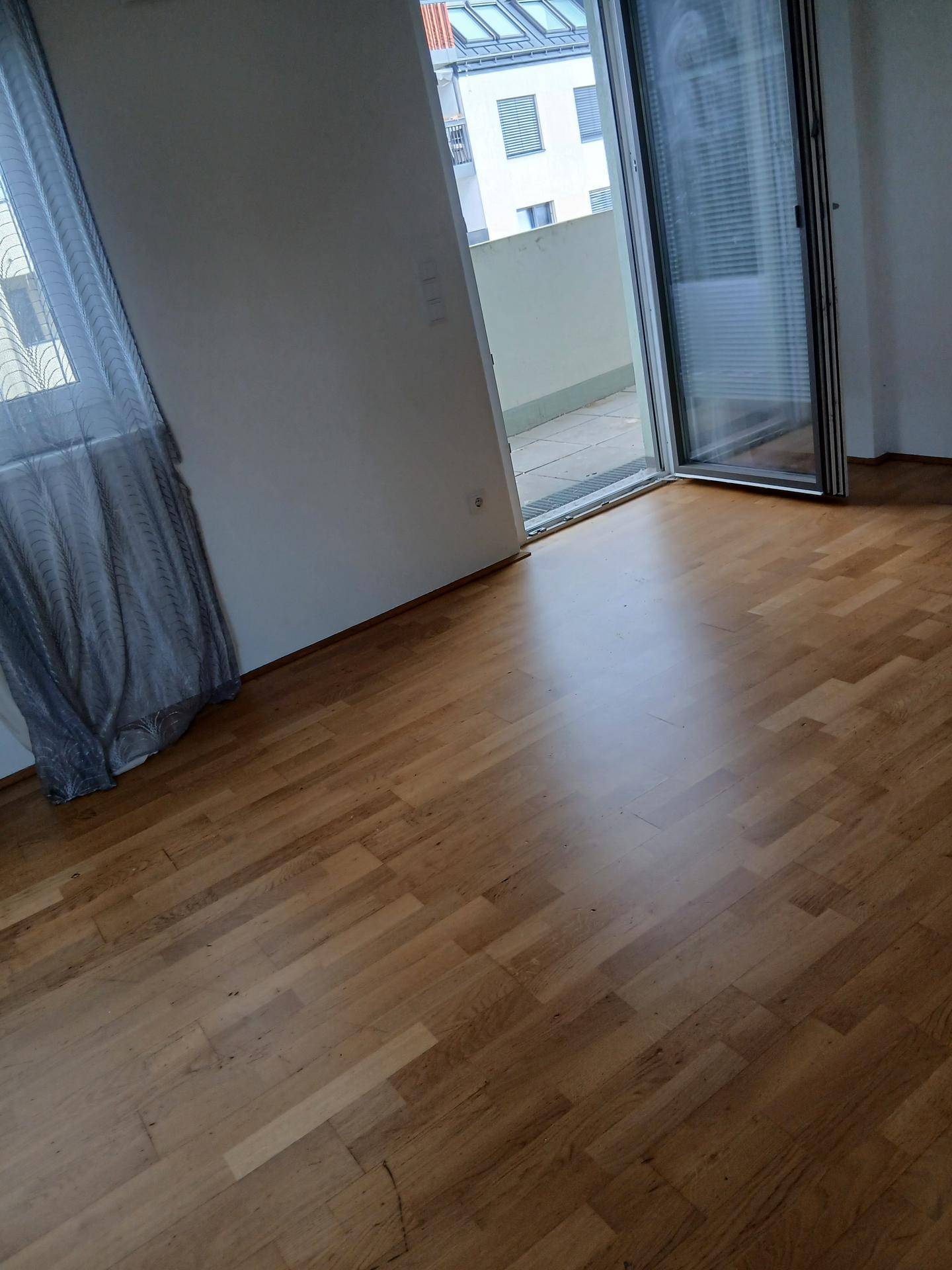 Geräumiges Zimmer mit Holzboden und Schiebetür zum Balkon, das viel Tageslicht bietet.