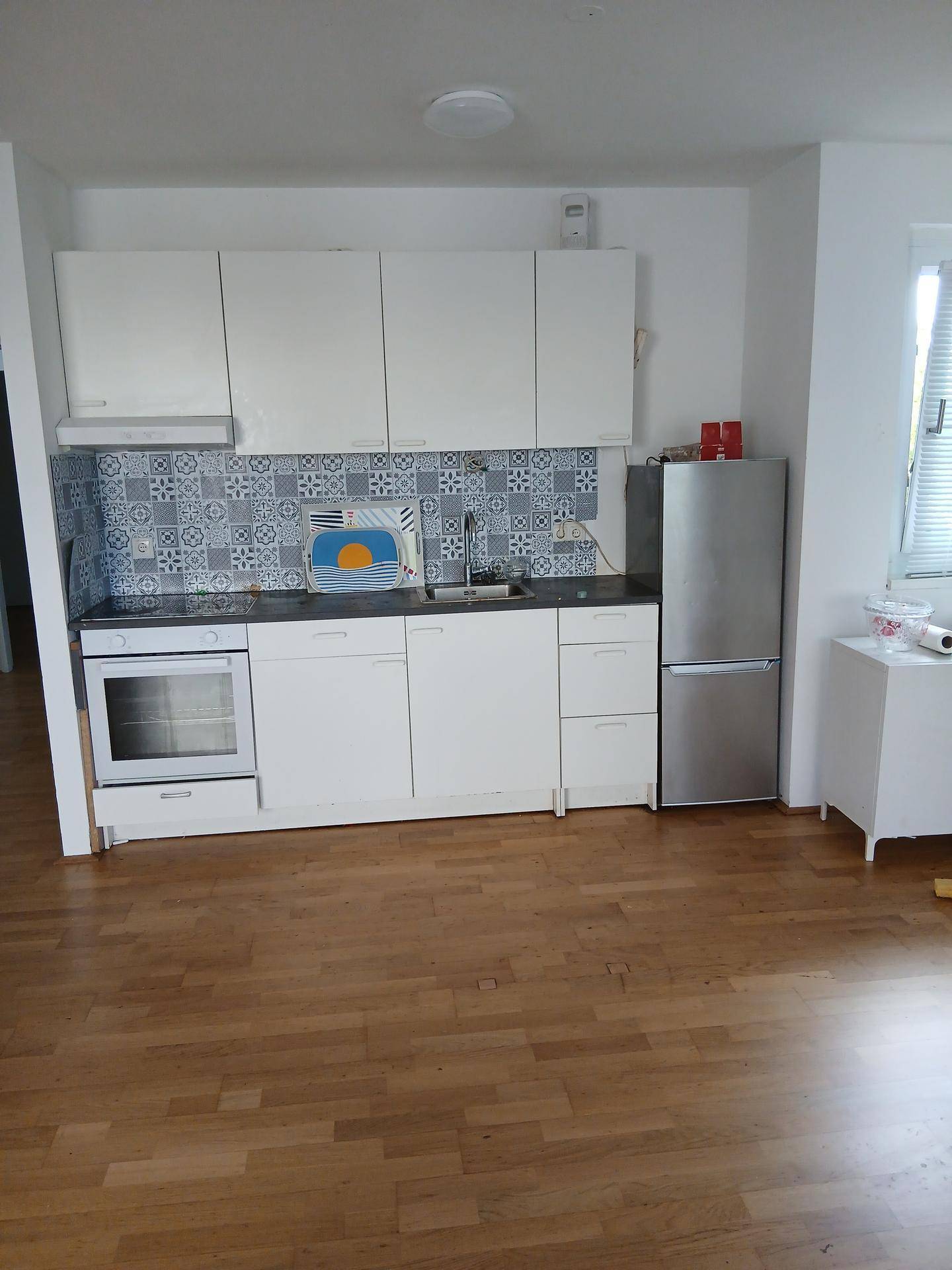 Funktionale Küche mit weißen Oberschränken, Herd und Kühlschrank, gut beleuchtet.