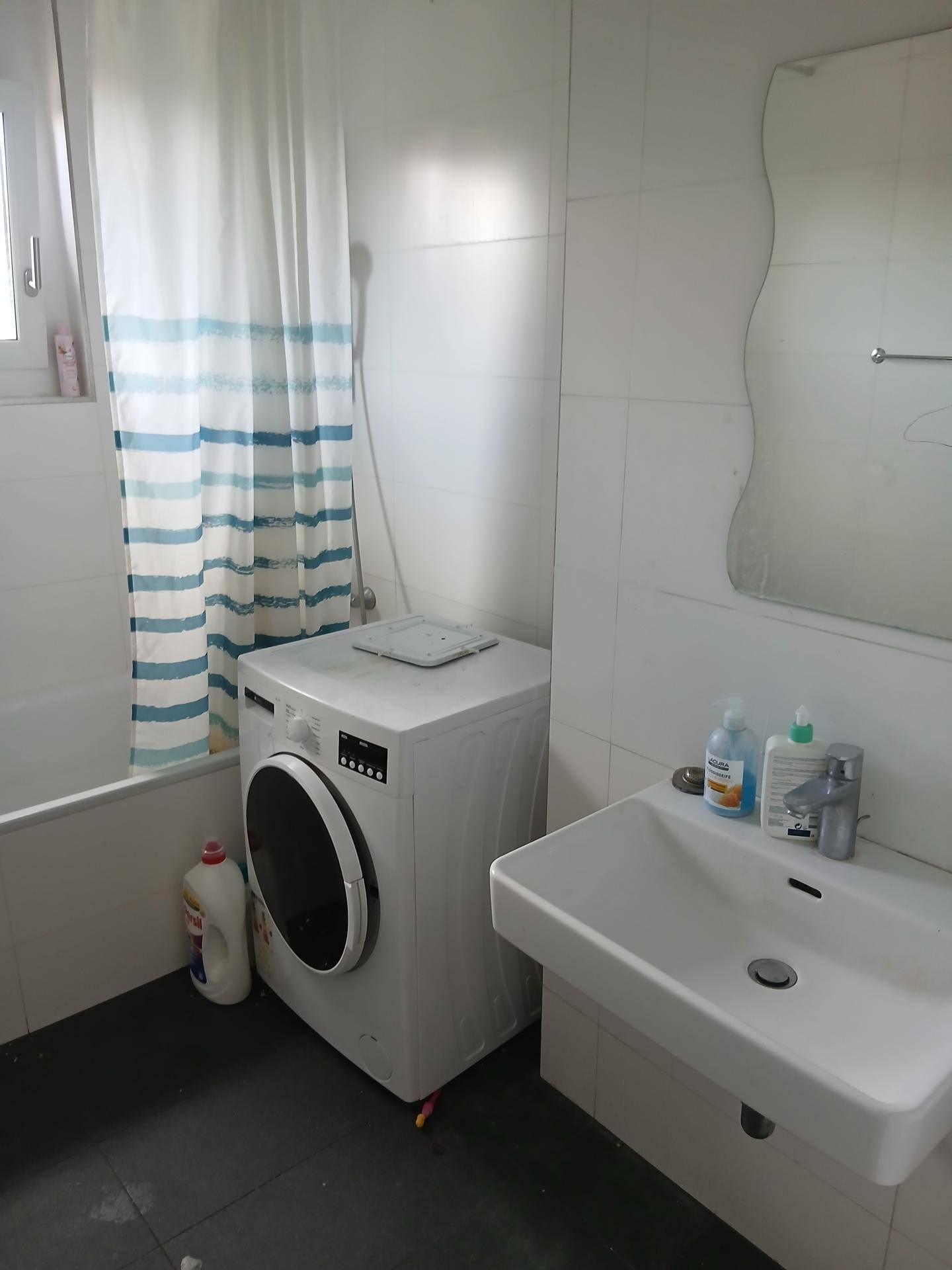 Badezimmer mit Badewanne, Waschmaschine und weiß gefliesten Wänden.