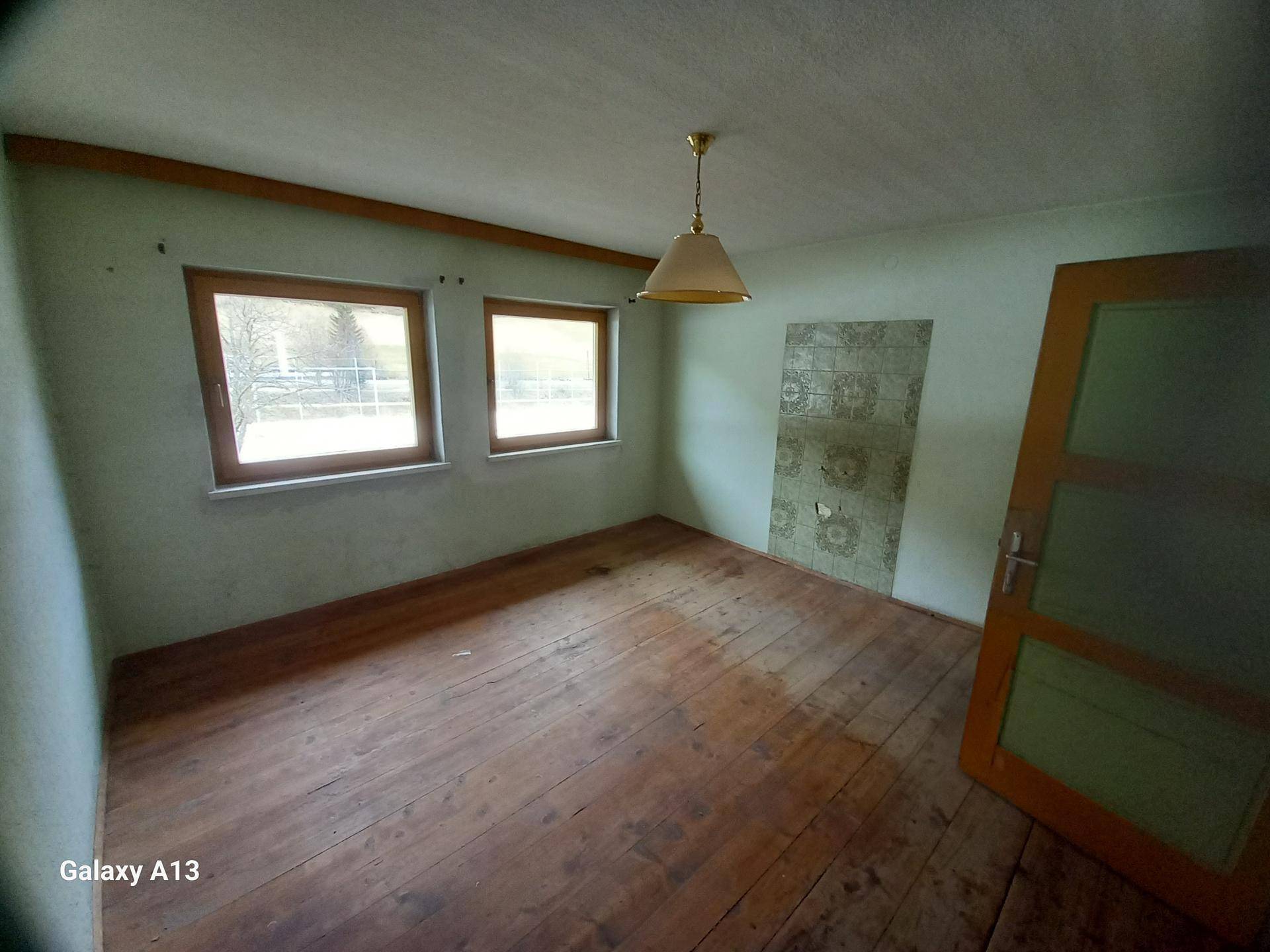Leeres Zimmer mit Holzboden, zwei Fenstern und einer Tür, bereit zur Renovierung.