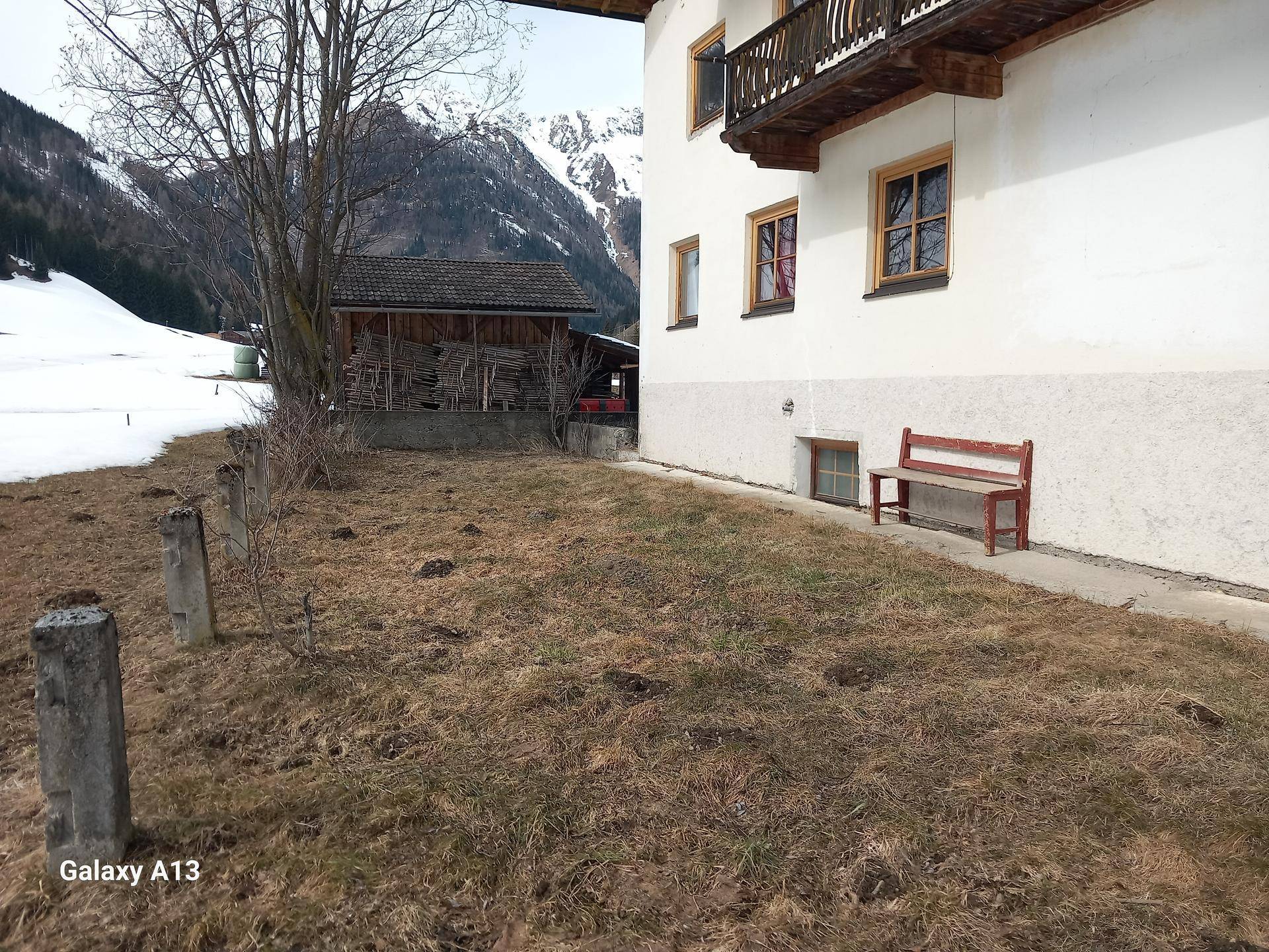 Seitlicher Blick auf das Haus mit einem kleinen Gartenbereich und einer Holzbank im Vordergrund.