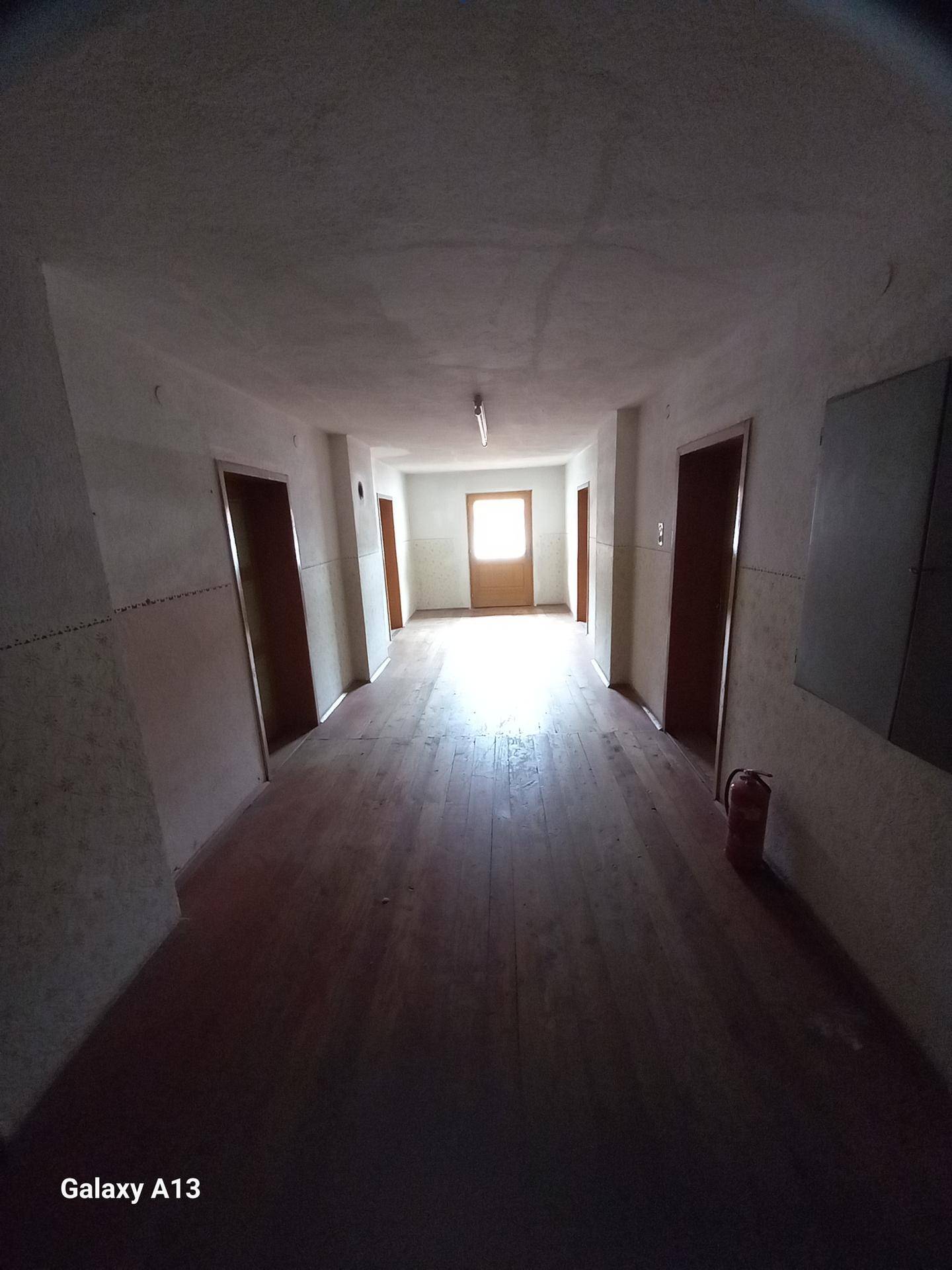 Langer Flur mit Holzboden und Türen, der zu einem hellen Ausgang am Ende führt.