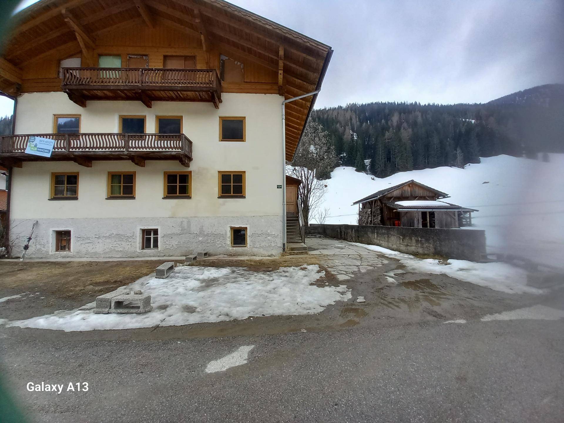 Traditionelles Haus mit Holzbalkonen und einem verschneiten Vorplatz in alpiner Umgebung.