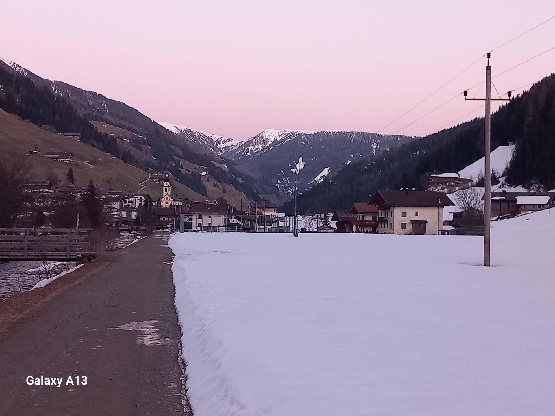 Malerisches Dorf in einem verschneiten Tal, umgeben von Bergen unter einem rosa Abendhimmel.