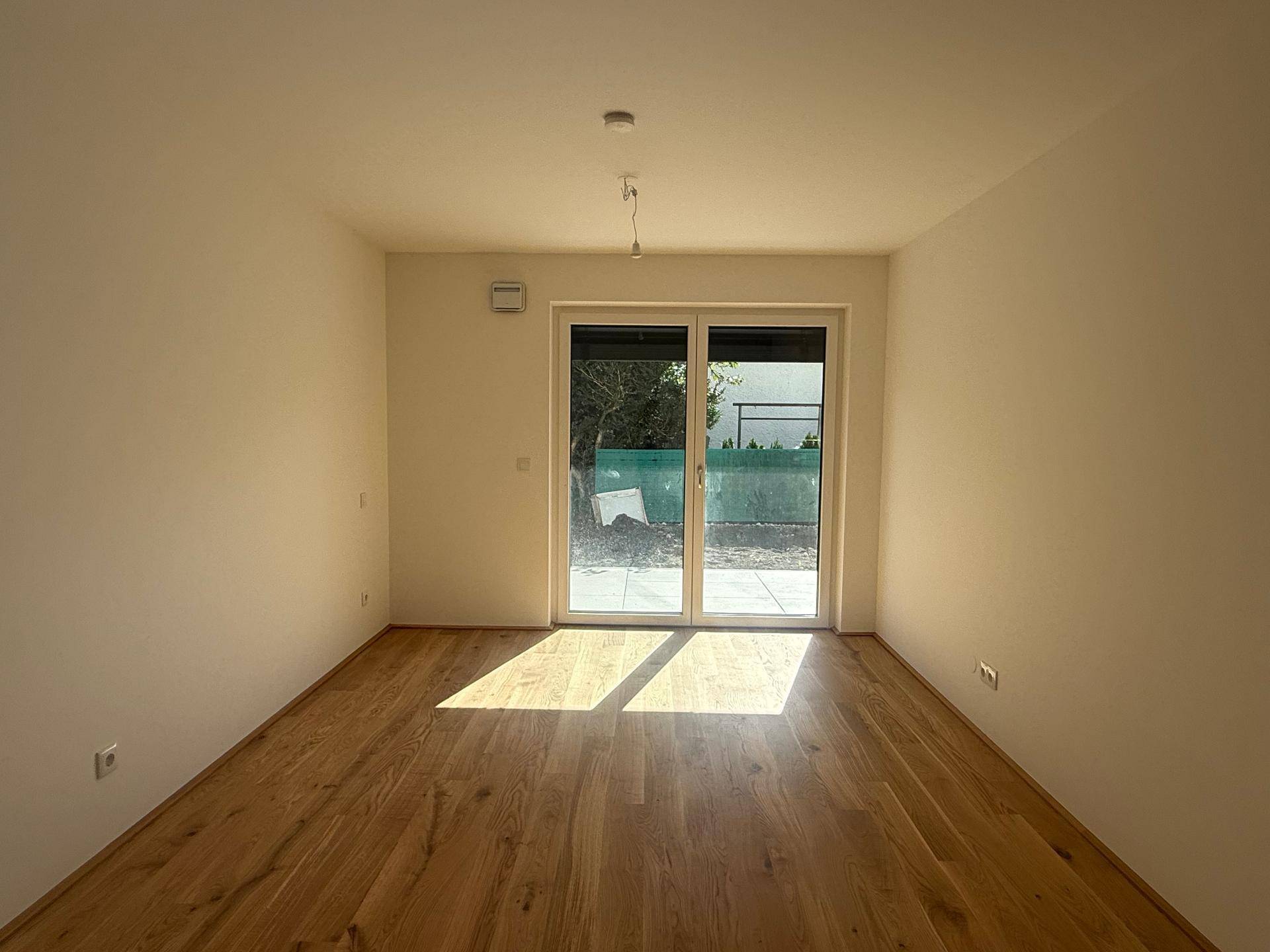 Helles Zimmer mit Parkettboden und großer Schiebetür, die viel Tageslicht hereinlässt.