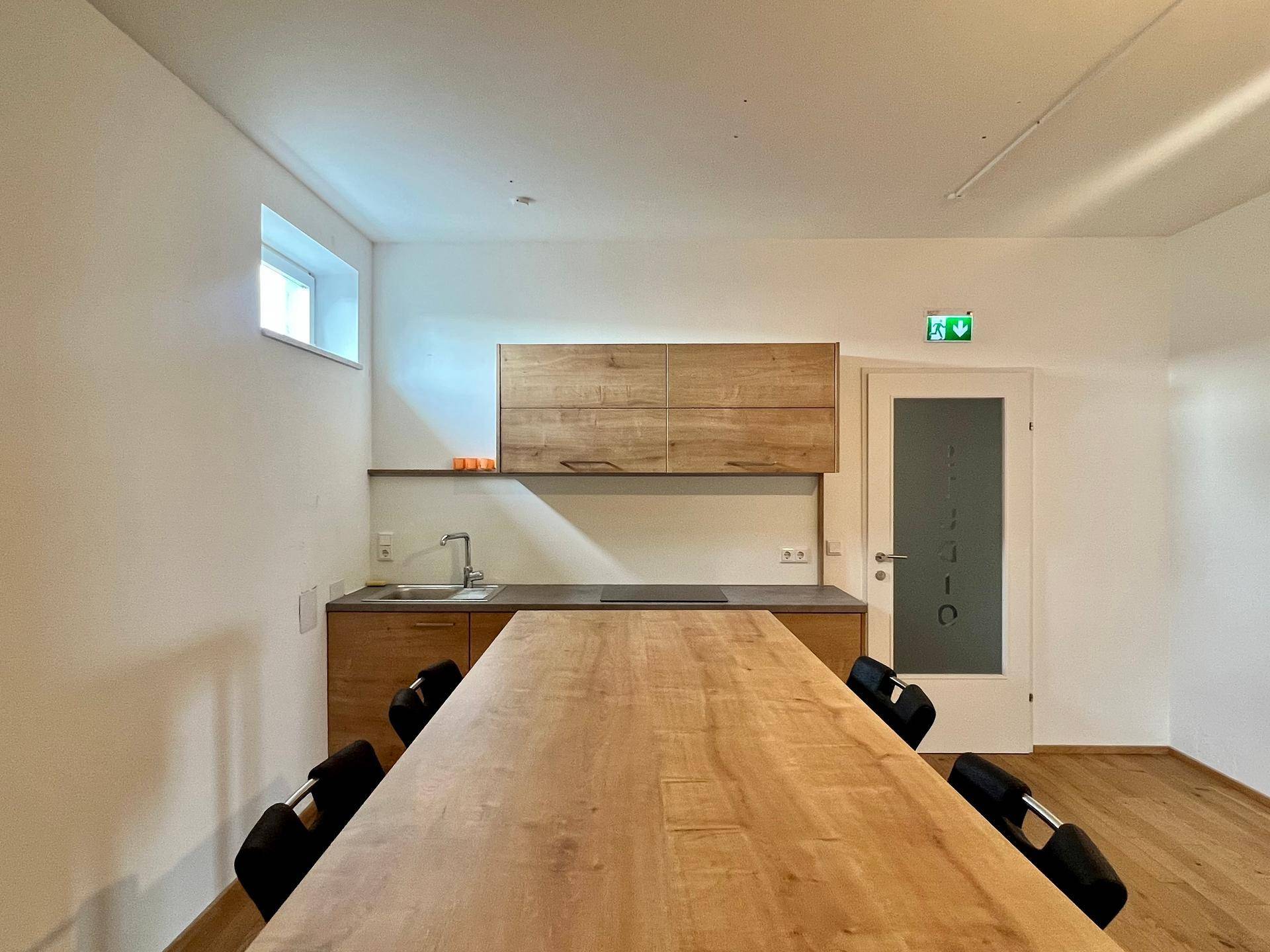 Funktionale Teeküche mit Holzfronten, Spüle und Induktionskochfeld, ideal für kurze Pausen im Büroalltag.