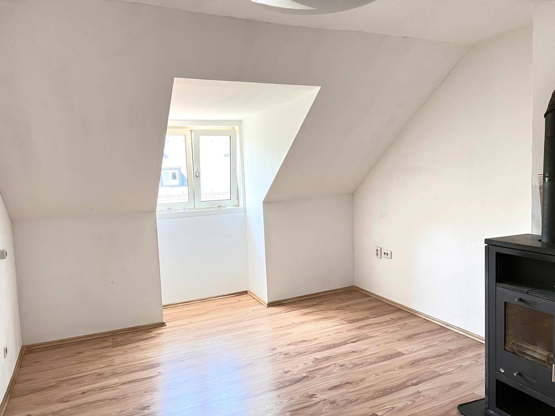 Gemütlicher Wohnraum mit Laminatboden, Dachschräge und einem Holzofen.