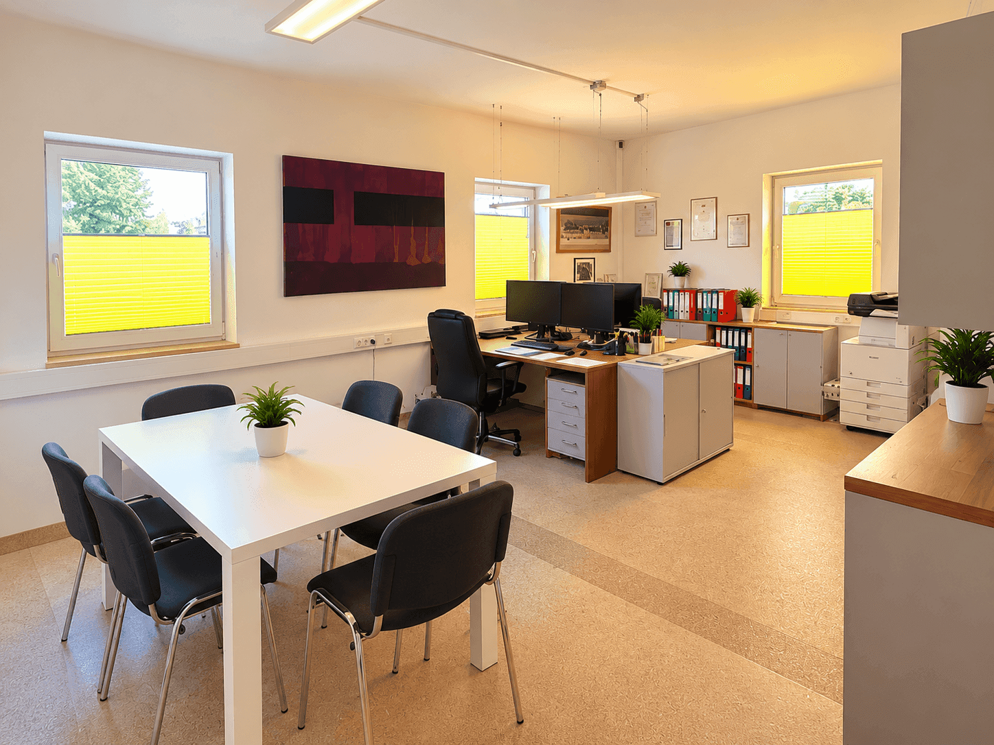 Geräumiges Büro mit Besprechungstisch, mehreren Arbeitsplätzen und großen Fenstern mit gelben Plissees.