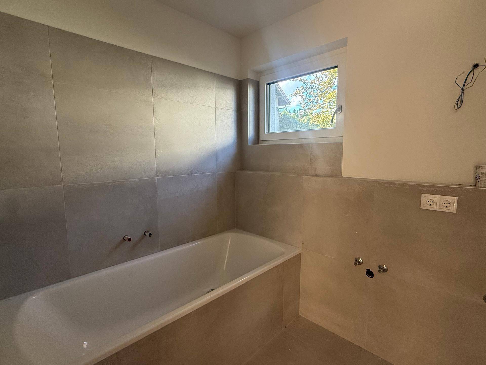 Modernes Badezimmer mit Badewanne, großen Fliesen und Fenster für Tageslicht.