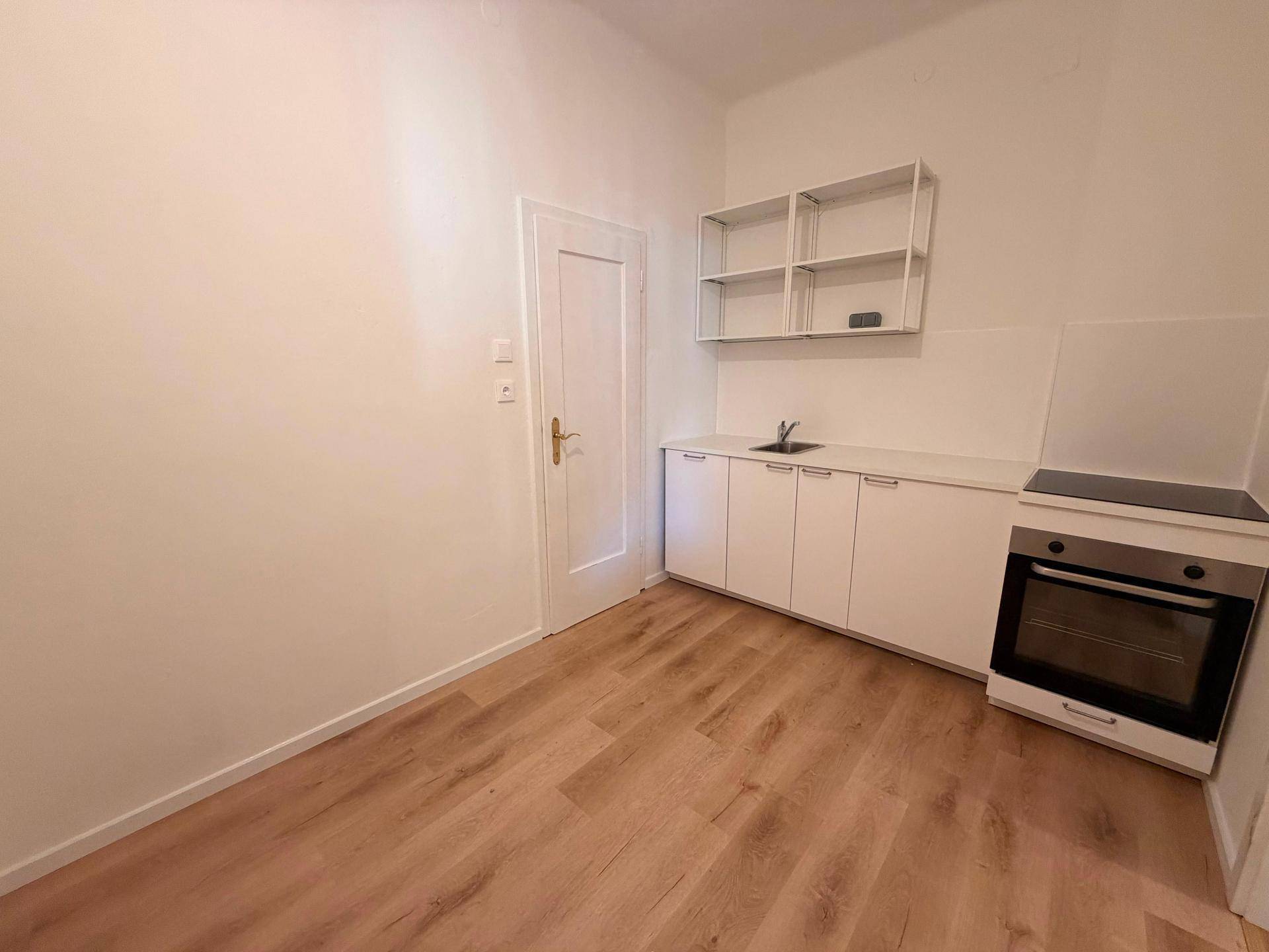 Kleine Küche mit weißen Schränken, Herd und Laminatboden, ideal für eine kompakte Wohneinheit.
