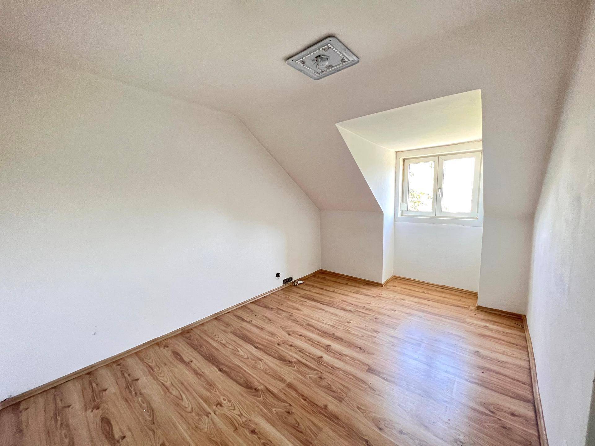 Leeres Zimmer mit Laminatboden, Dachschräge und Fenster für natürliches Licht.