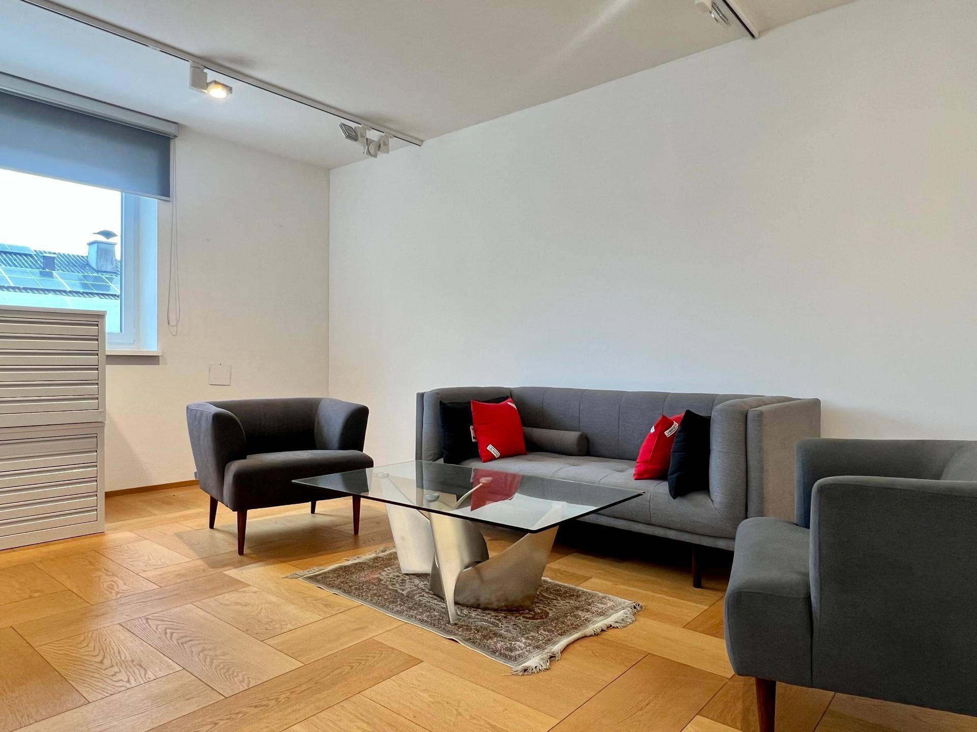 Einladende Lounge-Ecke mit modernem Sofa, Sesseln und Glastisch auf elegantem Holzparkettboden.