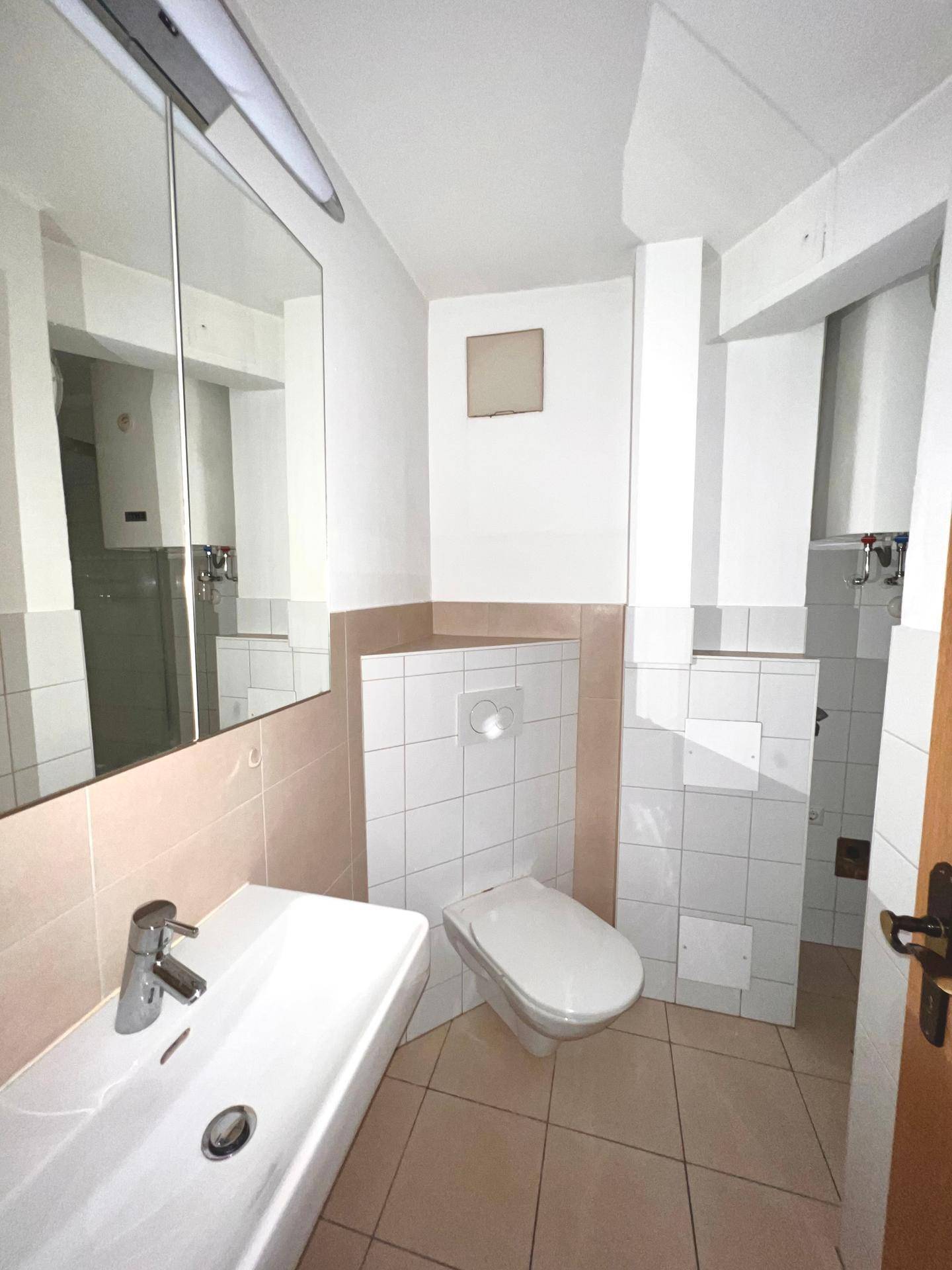 Funktionales Badezimmer mit Waschbecken, Toilette und Spiegelschrank.